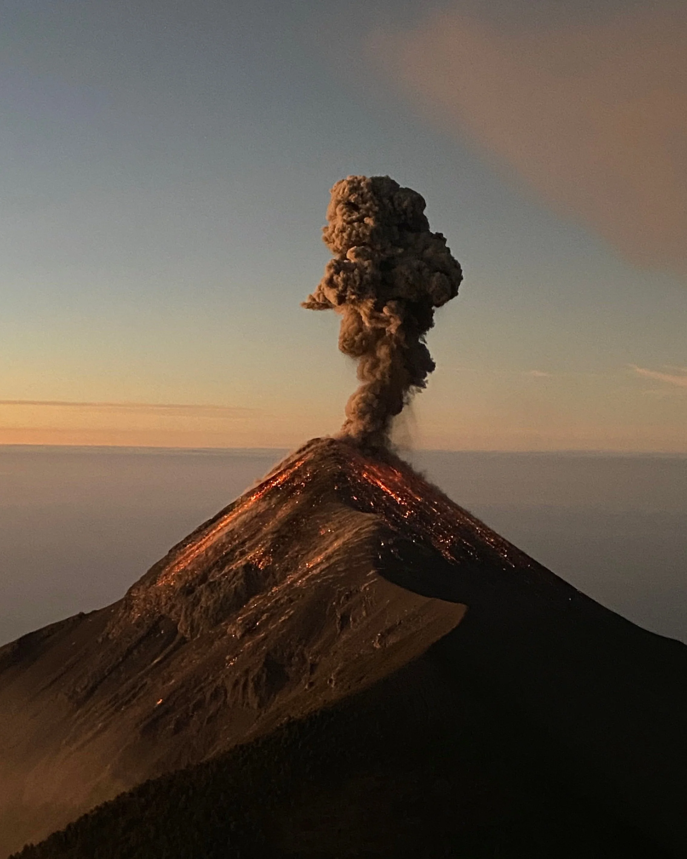 An erupting volcano spewing ash and smoke into the sky at sunset.