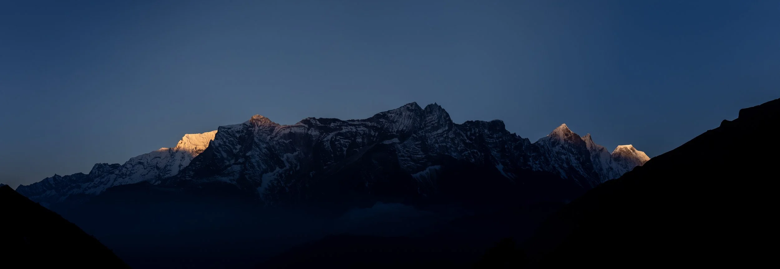 Snow-covered mountain peaks during sunrise or sunset with a clear blue sky.