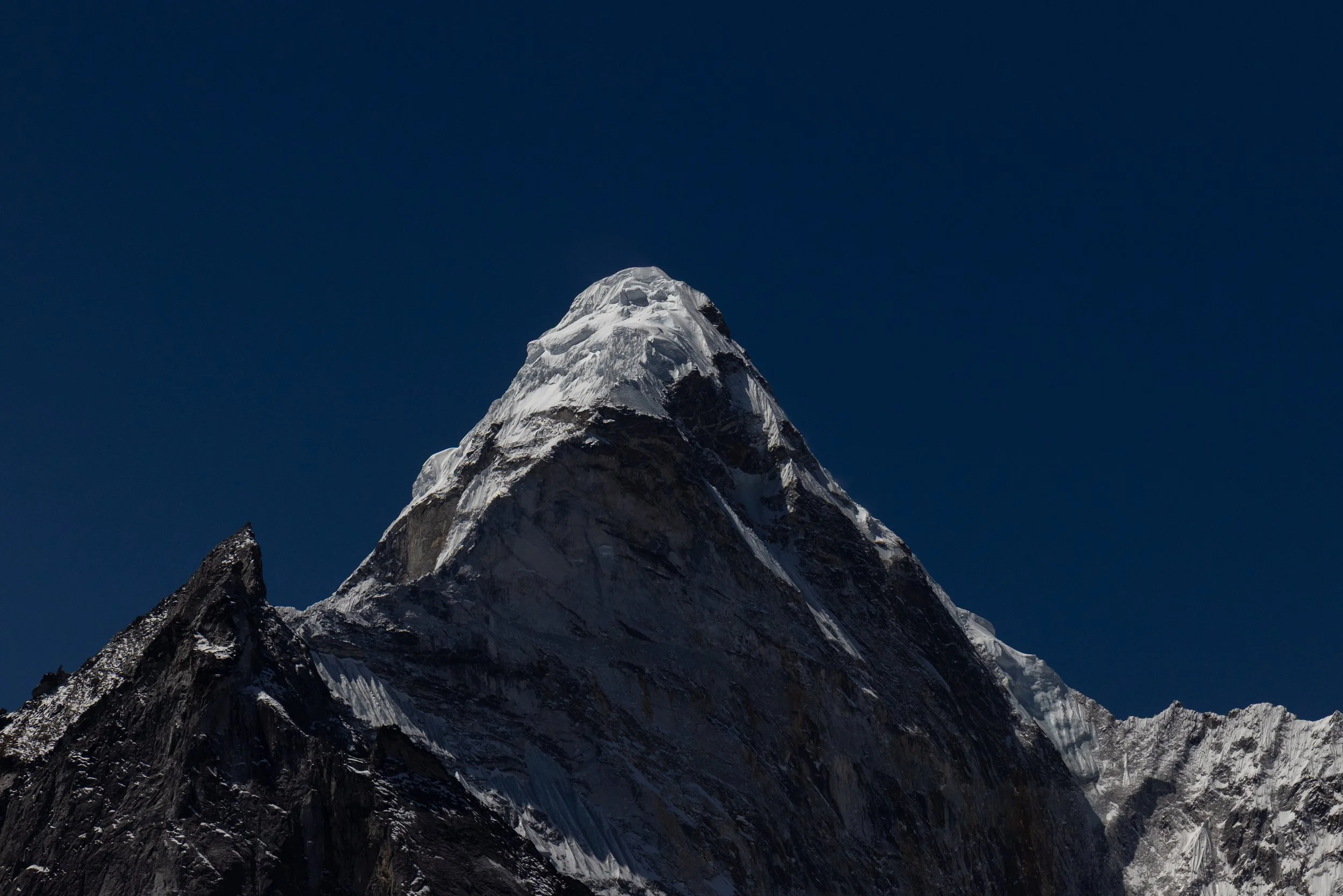 A tall, snow-covered mountain peak against a dark blue sky.