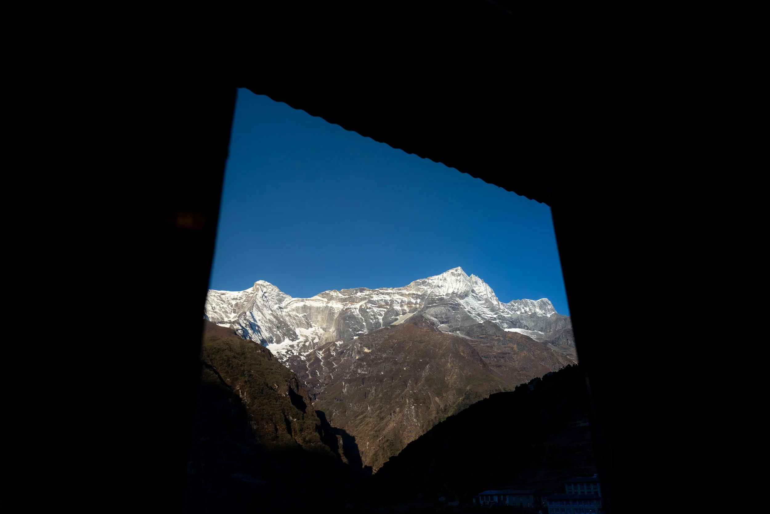 Snow-capped mountains seen through a rectangular window opening in darkness.