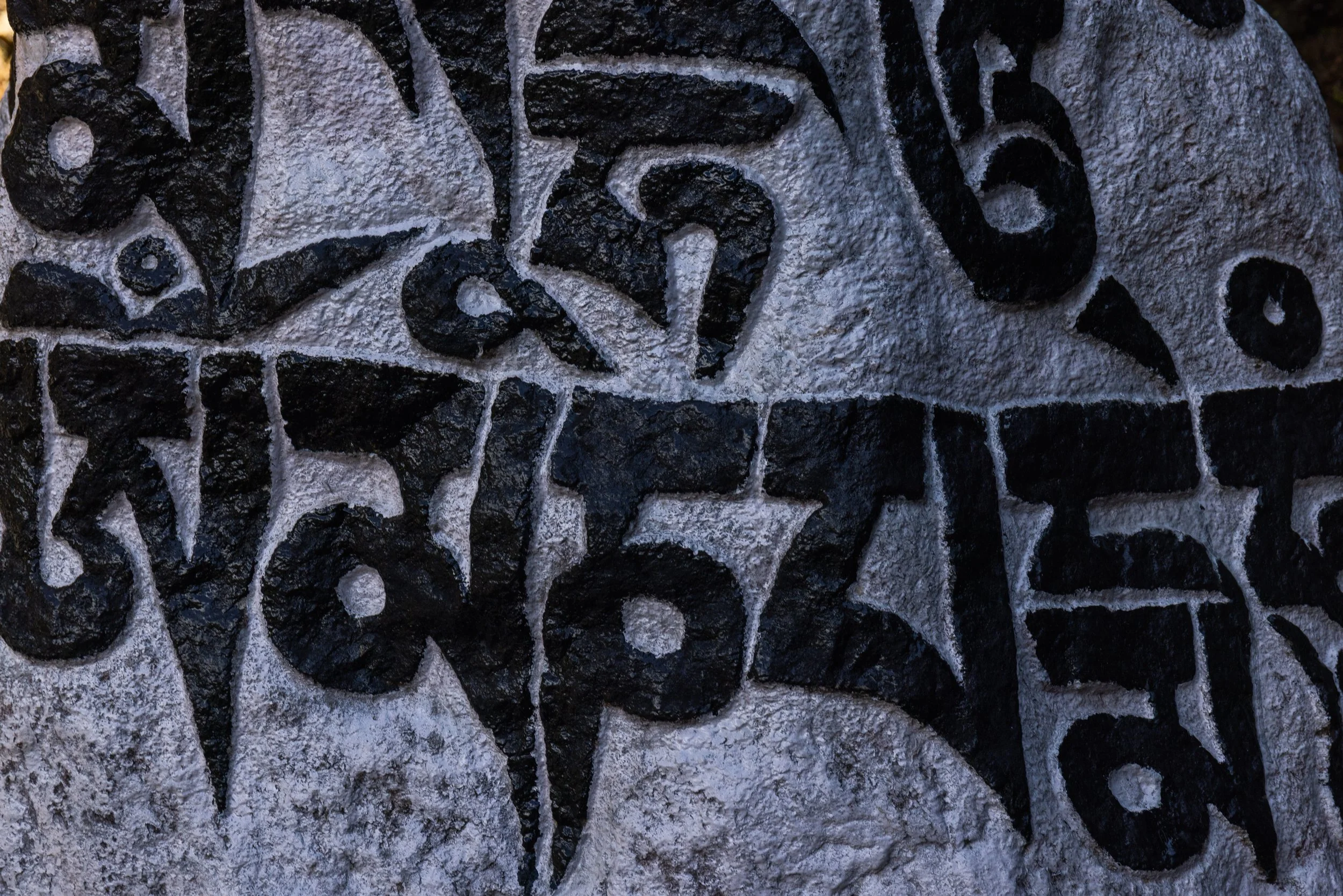 Close-up of carved black letters on a rough gray stone surface.