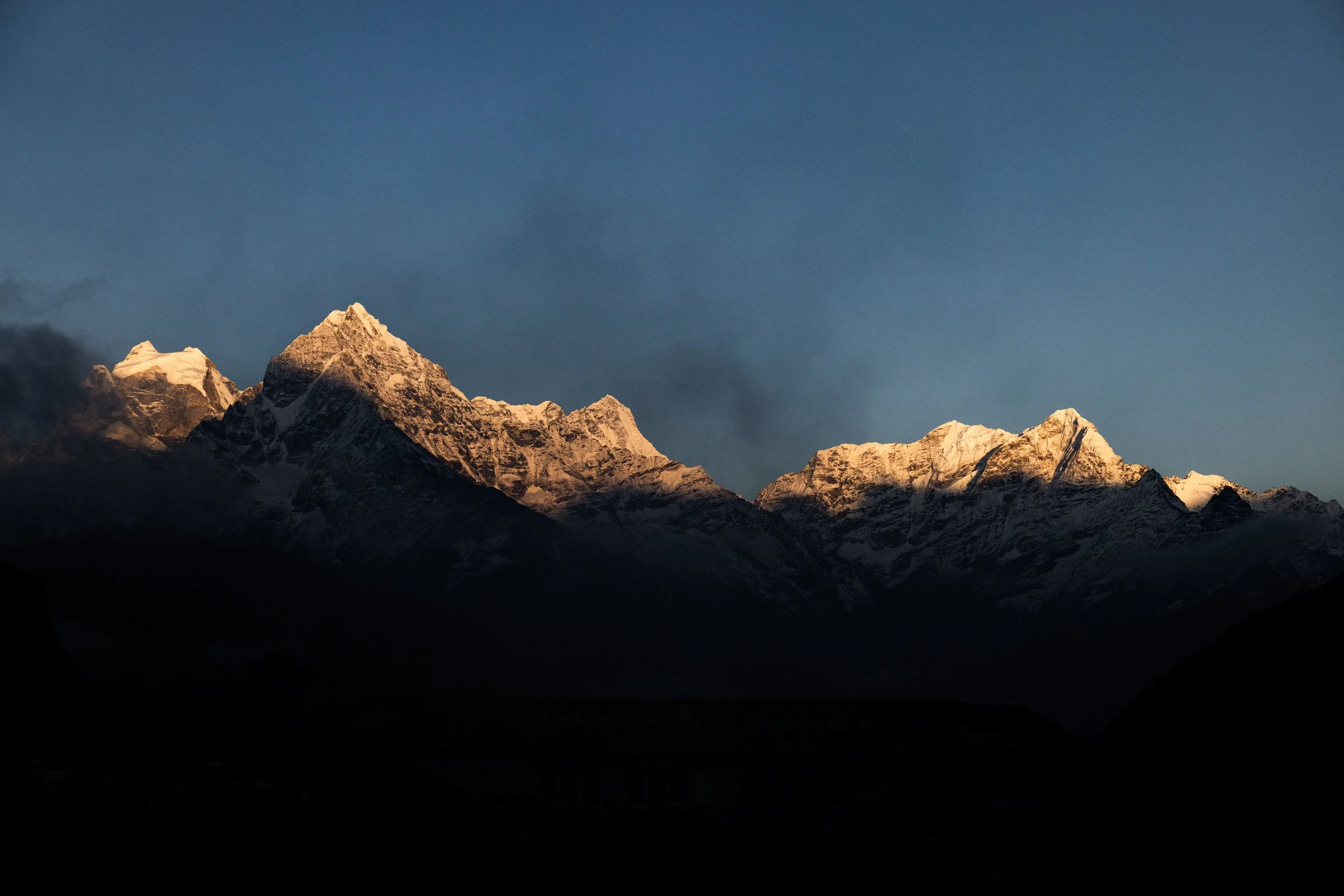 Snow-capped mountain peaks illuminated by sunlight against a dark sky.