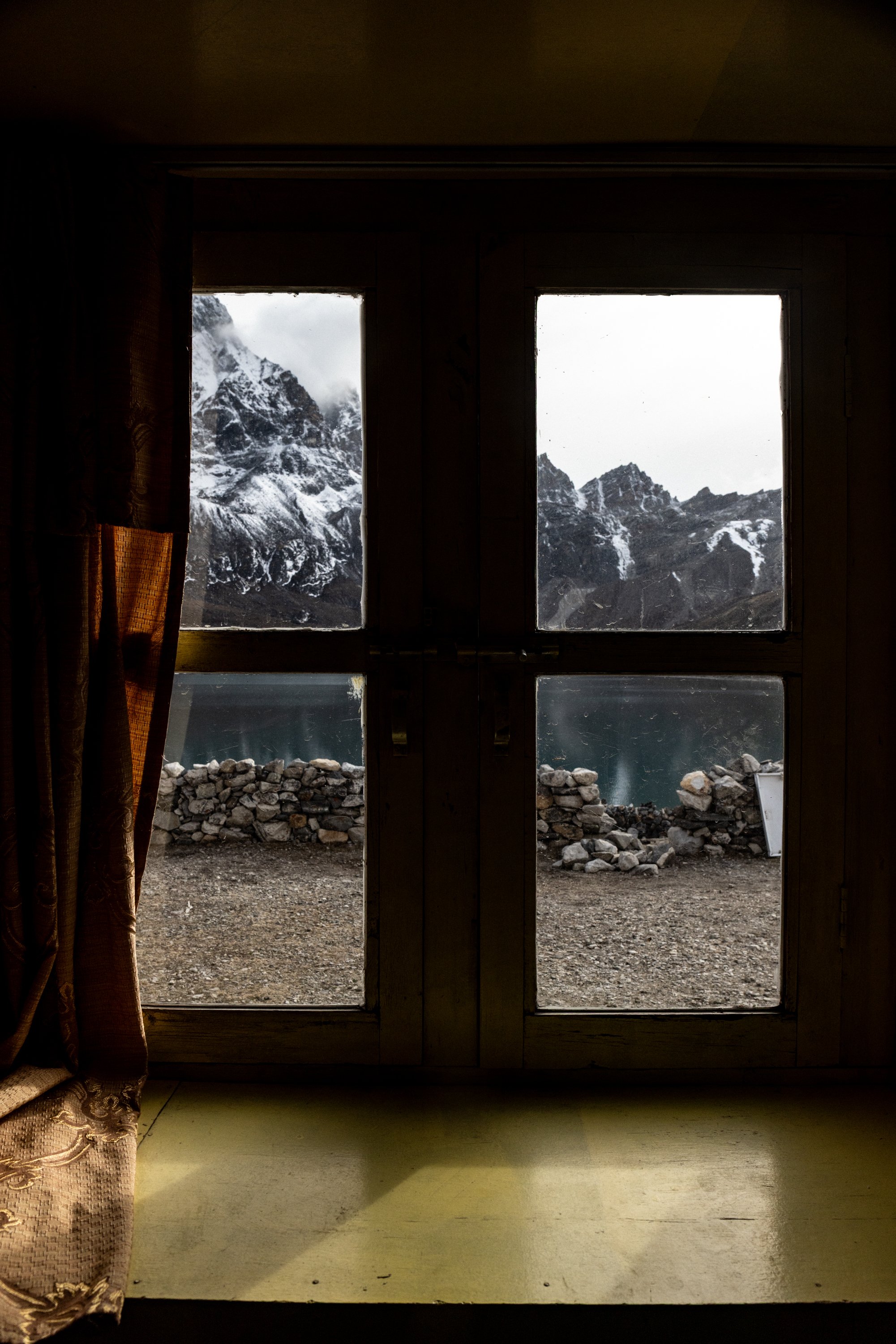 View of snow-capped mountains and a lake seen through a wooden framed window with glass panes.