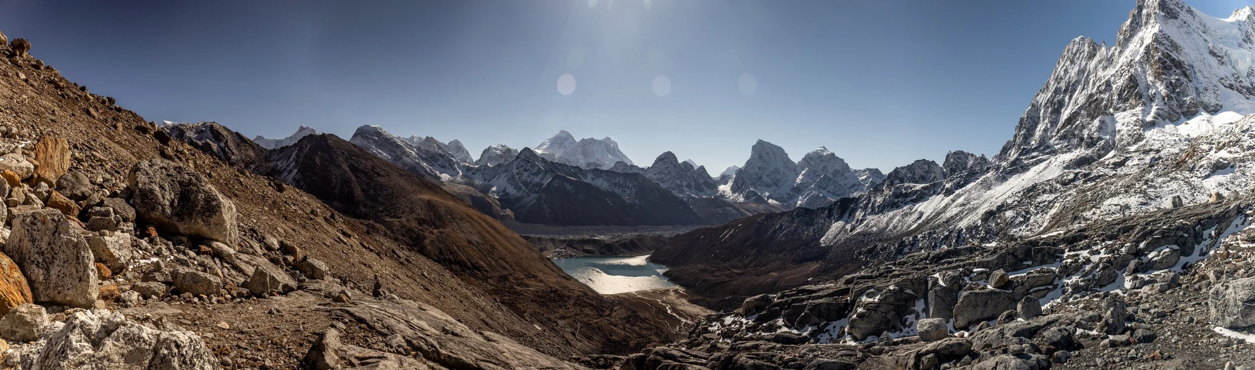 Snow-capped mountains with rocky slopes and a small lake at the valley in the foreground.