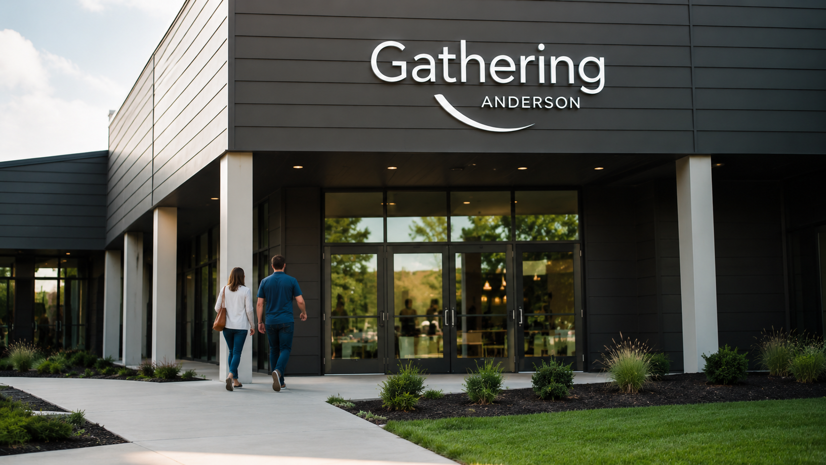 Two people walking into a modern building with a sign that says 'Gathering Anderson'.