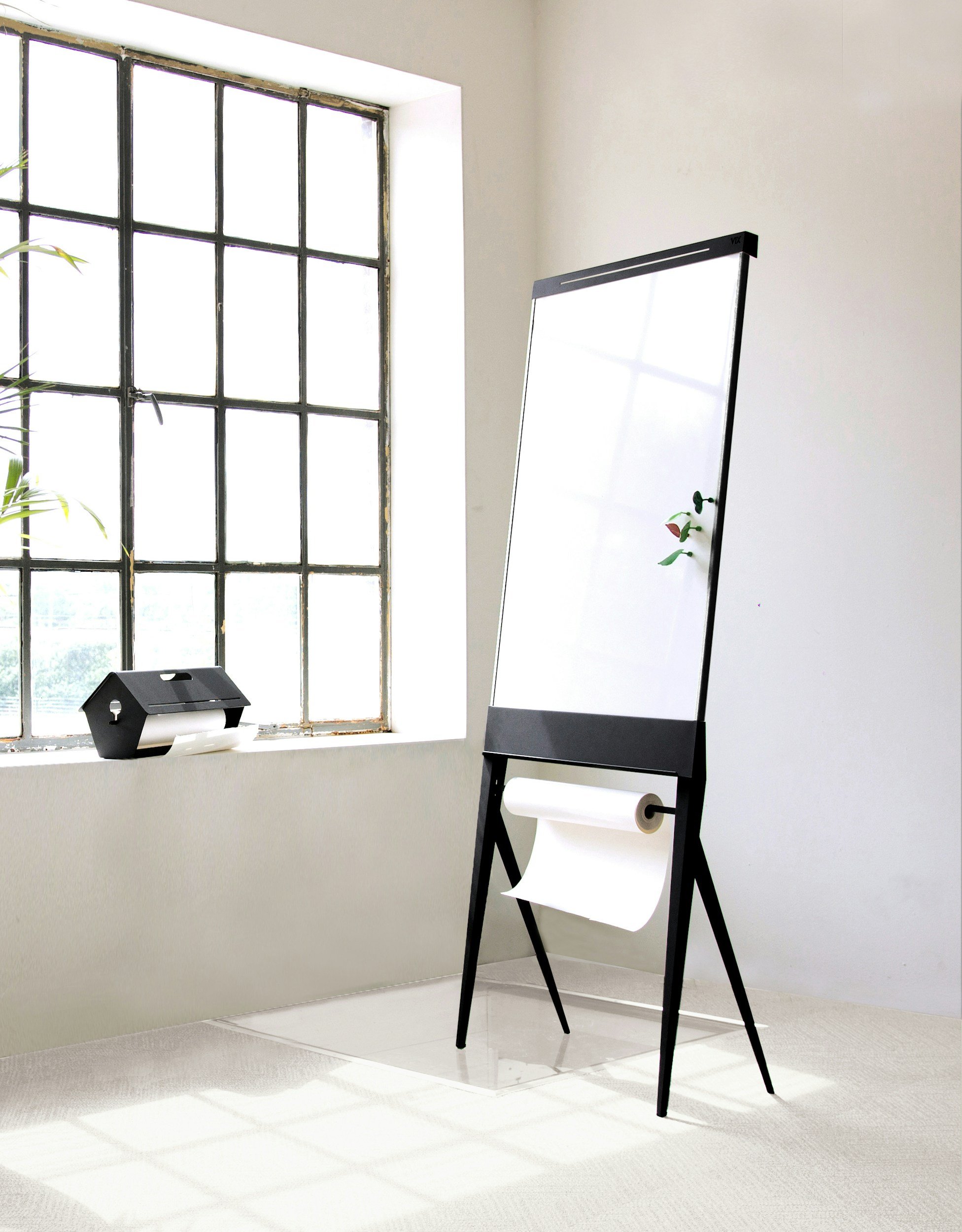 Ein Flipchart auf schwarzem Metallständer in einem hellen, ruhigen Raum mit großem Sprossenfenster – Symbol für professionelle Fortbildungsarbeit und gemeinsames Erarbeiten in Teamworkshops.