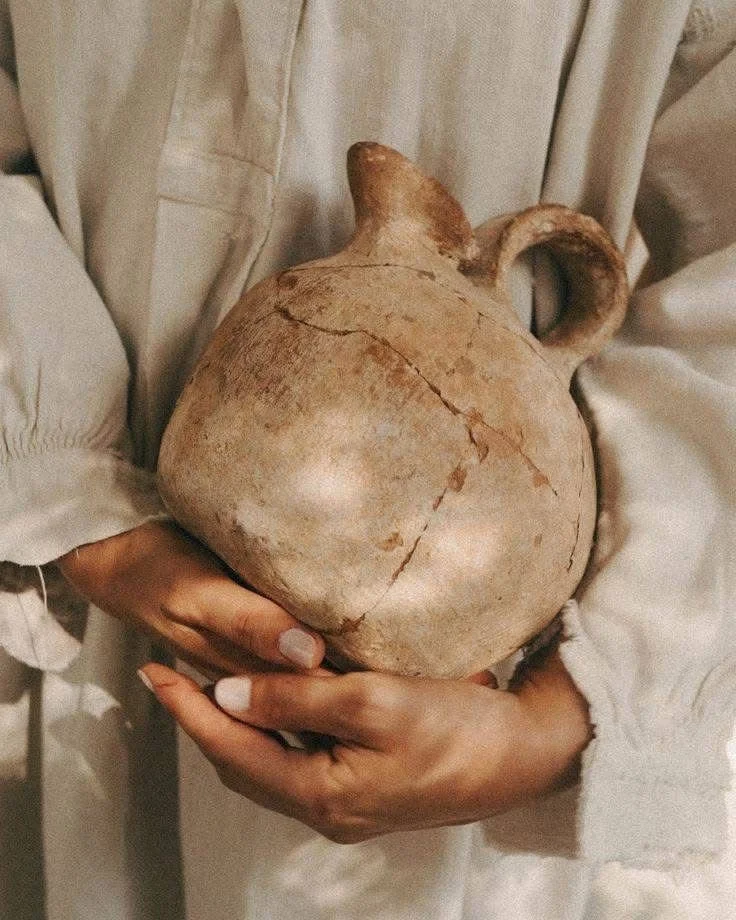 Person holding a large, ancient clay vessel or jar with cracks and an irregular shape.