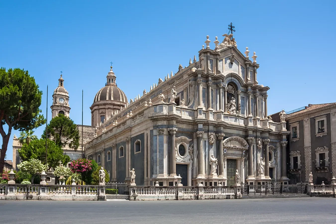 Chiesa barocca in stile italiano con decorazioni ornate, statue e un campanile in pietra, situata su una strada cittadina soleggiata