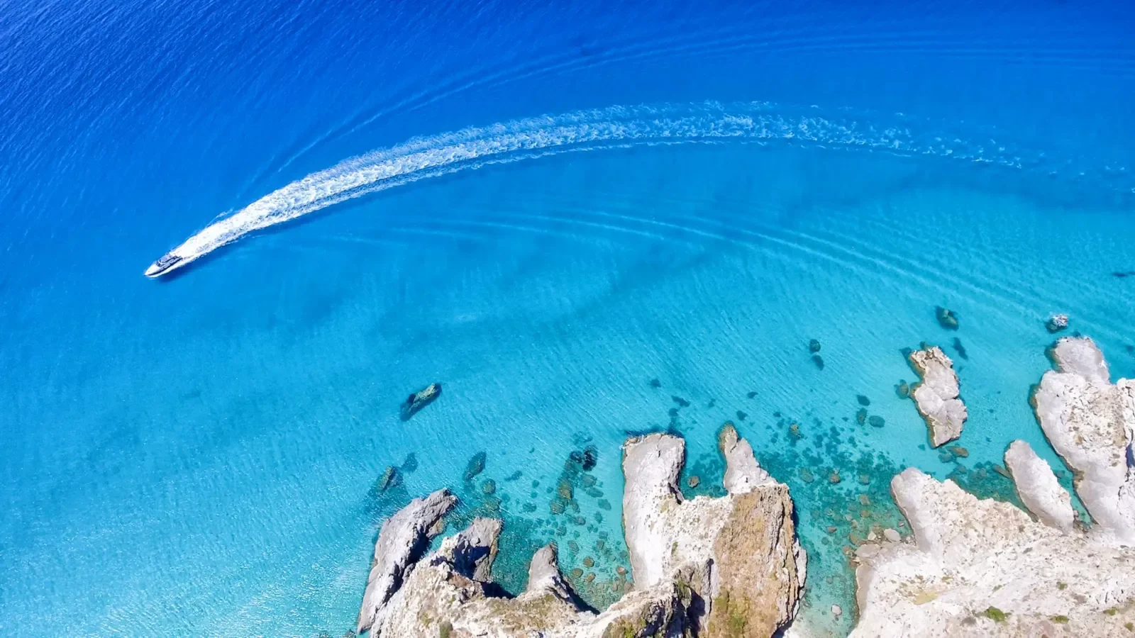 Sguardo aereo di una barca che naviga in acque turchesi vicino a scogliere delle Isole Egadi.