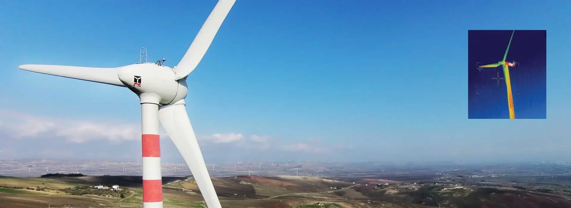 Un parco eolico con turbine eoliche bianchi e un cielo blu. Ingrandimento di una torre eolica in alto, con dispositivi di supporto e attrezzature sulla cima.