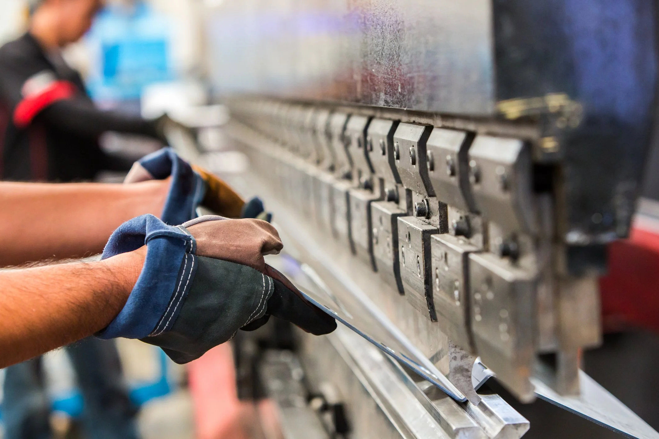 Worker's hands in gloves adjusting metal machine parts on an industrial manufacturing line.