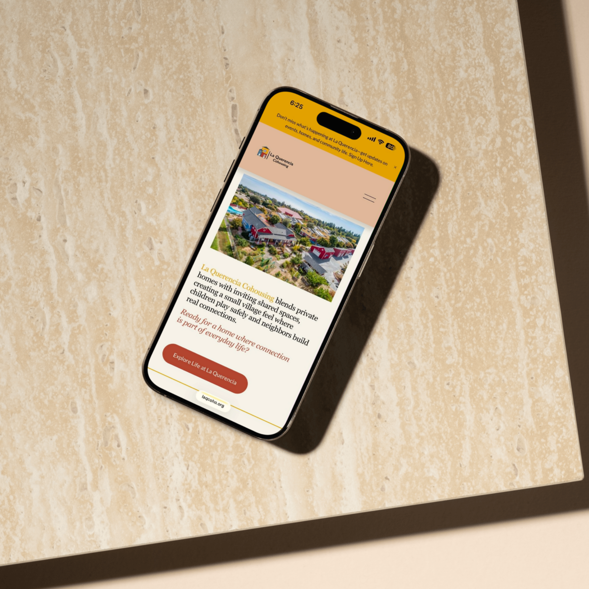 Smartphone placed on a beige marble table displaying a community website or app for La Quercia, with a scenic aerial photo of houses and a yellow header bar.