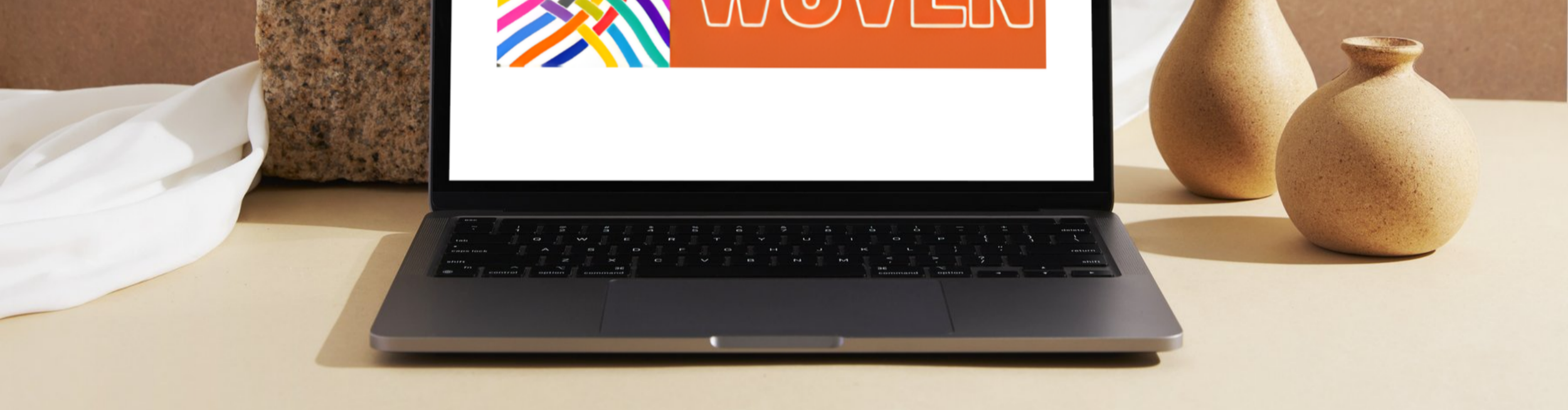 A laptop on a beige table with two vases in the background and a white cloth on the side.
