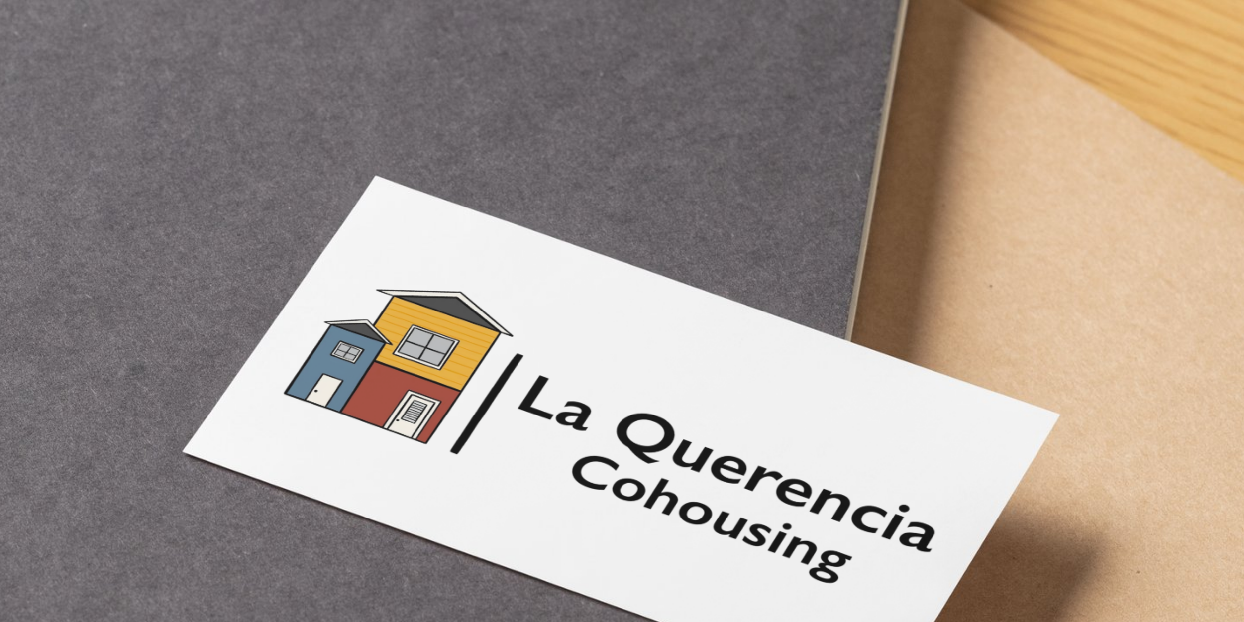 Close-up of a flyer featuring a colorful illustration of two houses and the text 'La Querencia Cohousing' on a table with a gray and tan surface.