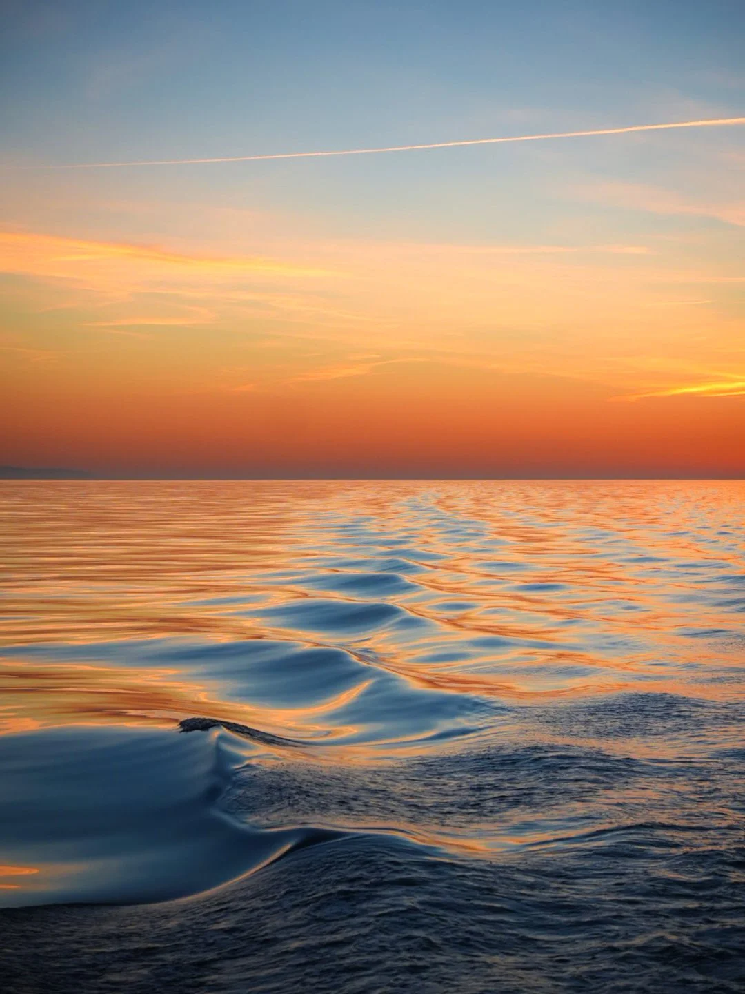Sunset over a calm ocean with colorful sky and gentle waves.