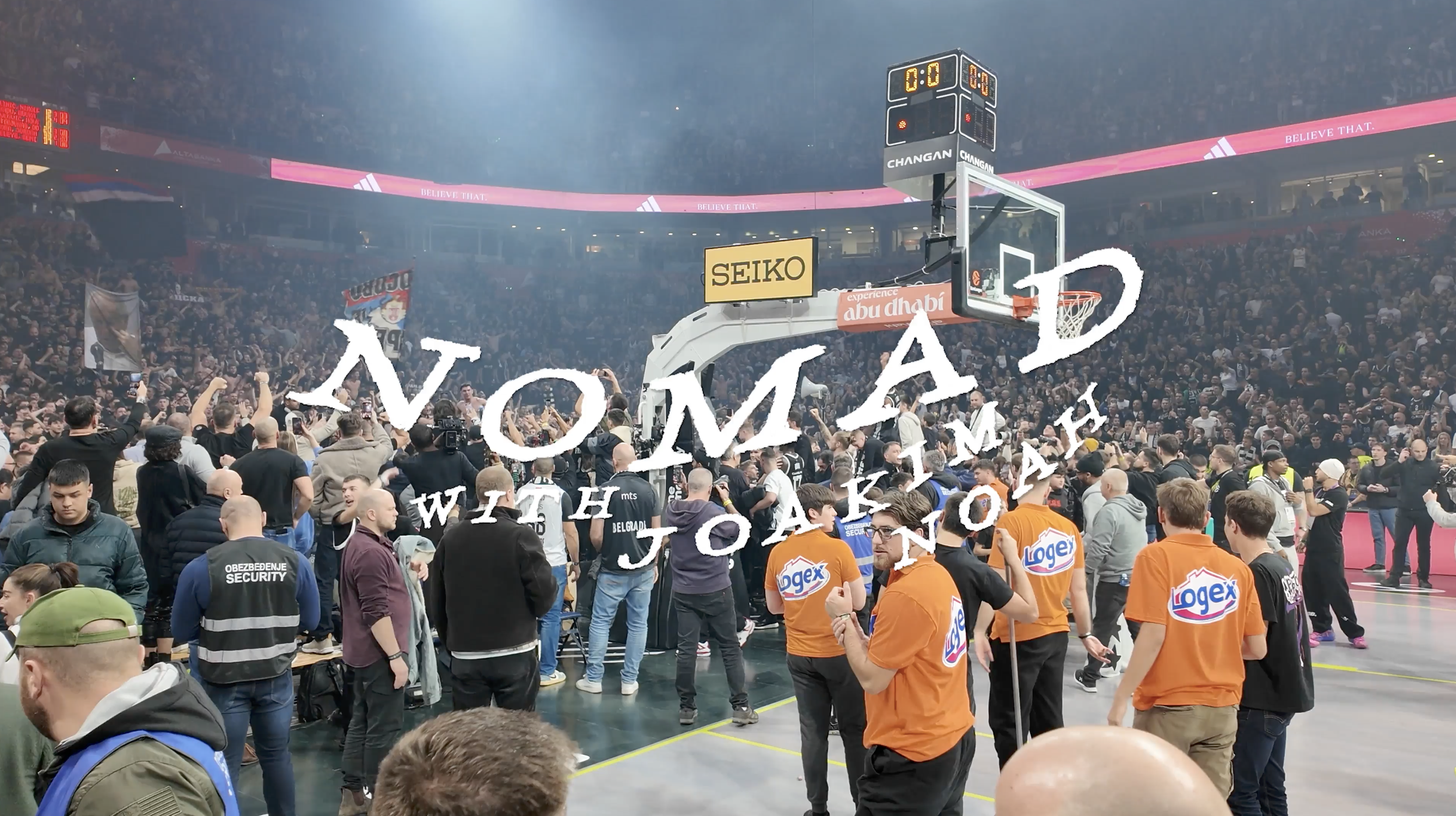 Crowd gathered in an indoor sports arena with a basketball hoop, scoreboard, and advertisements, celebrating an event or game.