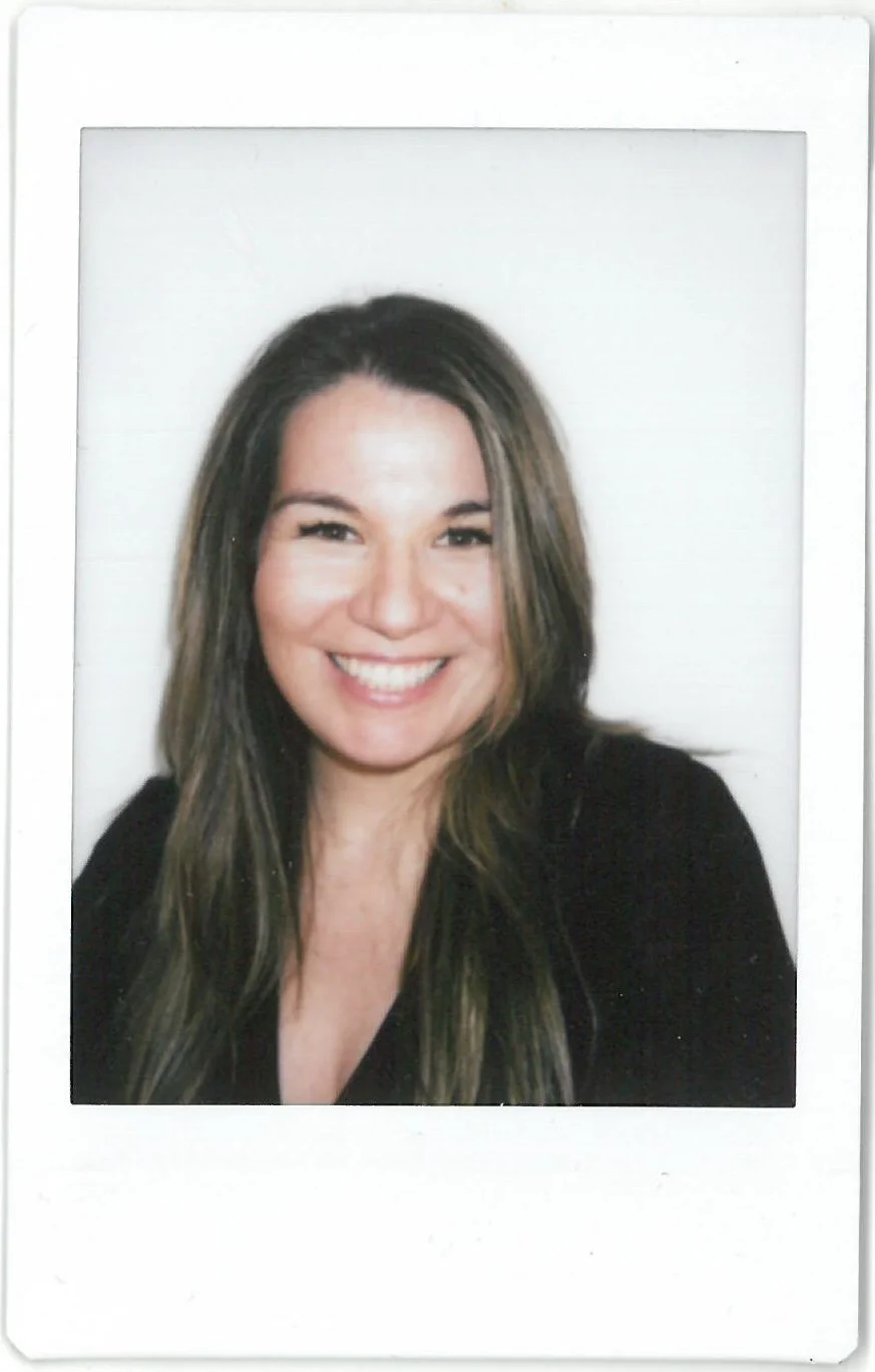 A woman with long brown hair smiling in a photo with a white background and a white border.
