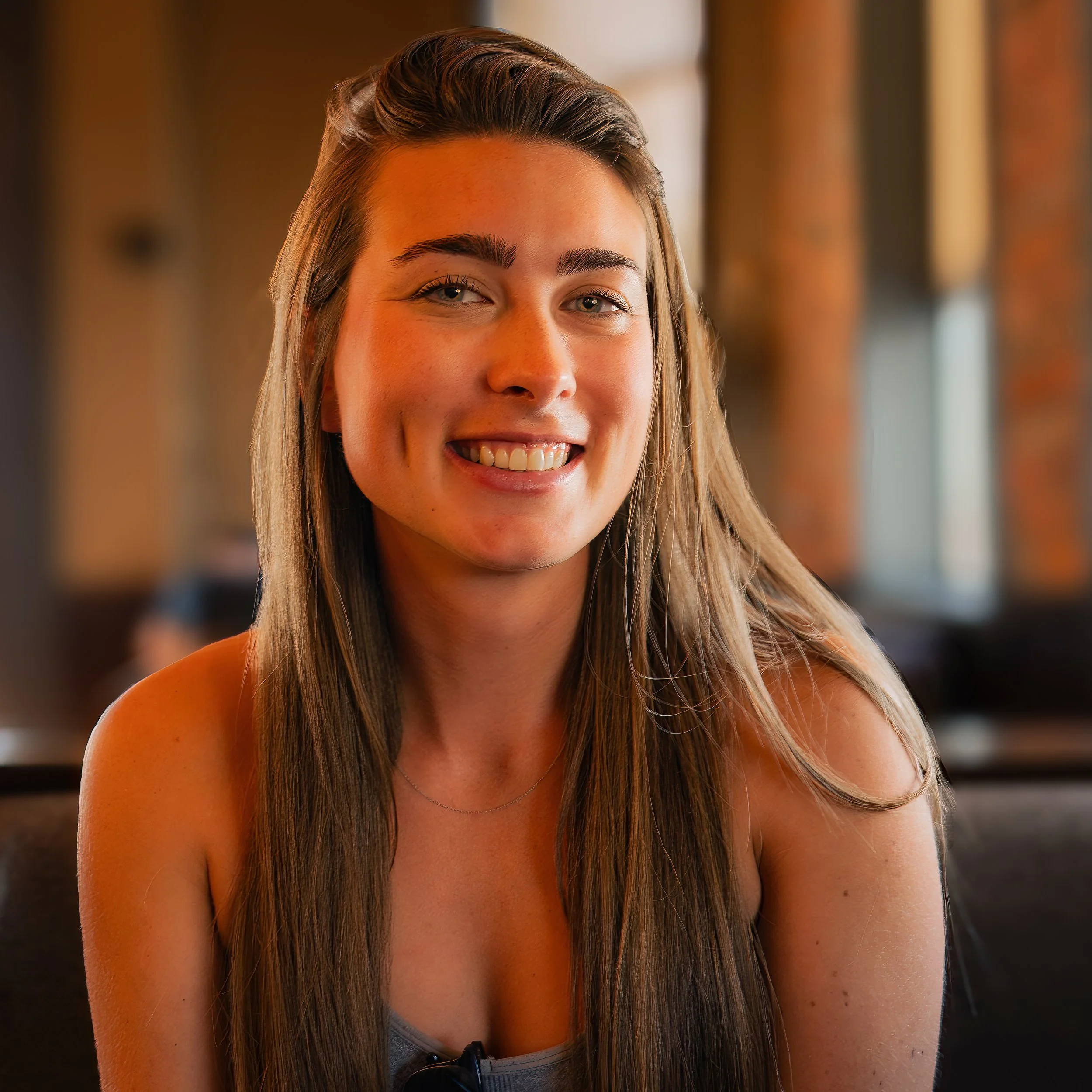 Close-up of a young woman with long, straight blonde hair smiling, with background blurred.