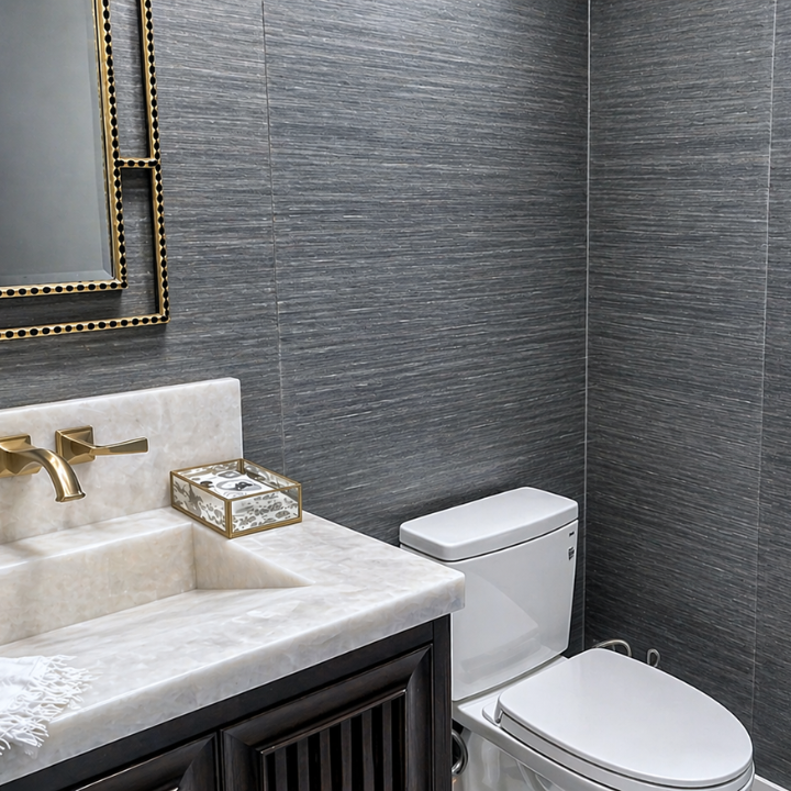 Modern bathroom with gray textured wall tiles, white toilet, and cream-colored marble sink with gold faucet.