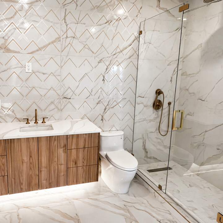 Modern bathroom with marble floors and walls, a wooden vanity with a marble countertop, a white toilet, and a glass-enclosed shower with gold fixtures.