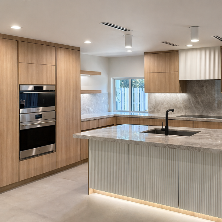 Modern kitchen with wooden cabinets, marble countertops, and a kitchen island with a black sink and faucet, under recessed lighting and a window with a fence outside.