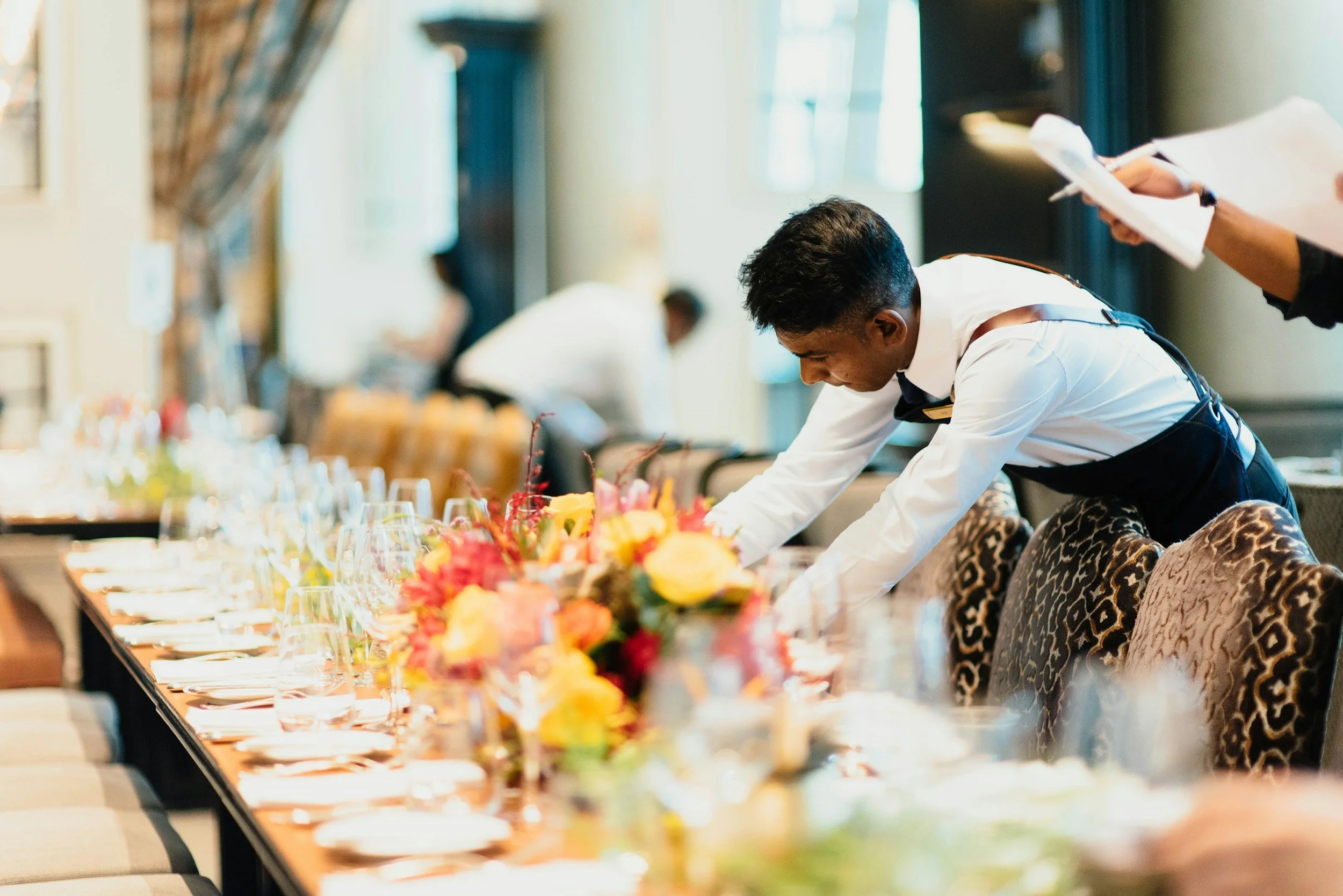 A waiter setting a banquet table with flowers in a restaurant or event hall.