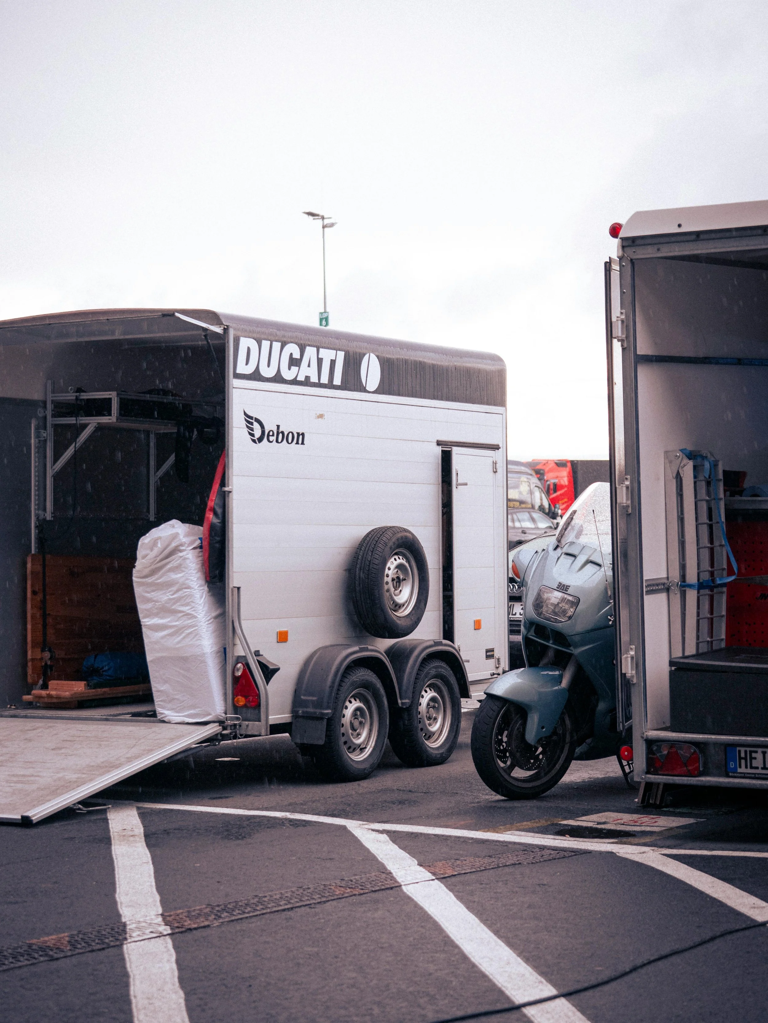 A parking lot with trailers, a motorcycle, and other vehicles. A trailer with the brand 'Ducati' is visible.