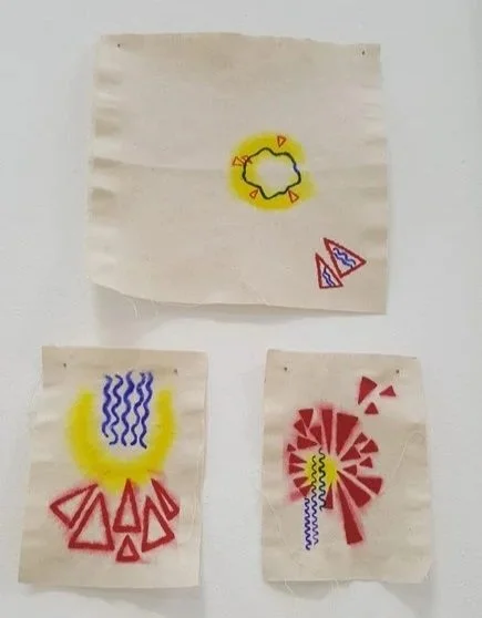 Three pieces of paper with colorful abstract doodles, including a yellow circle with red accents, a red geometric shape with blue zigzag lines, and a red sunburst with a yellow center and a blue wavy line.