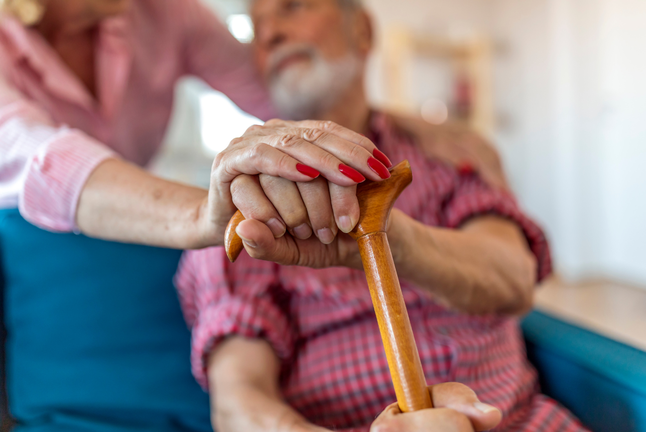 A senior woman supporting an elderly man with a cane at home.