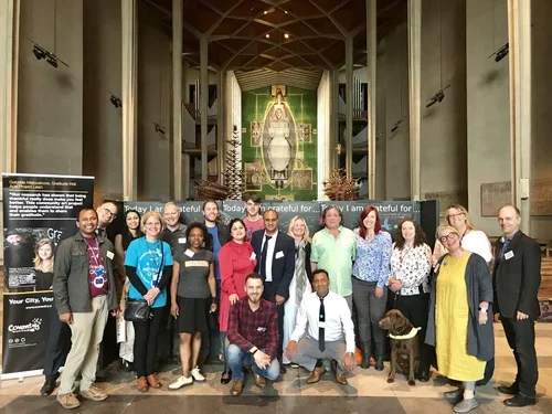 Group of diverse people posing in front of a large chalkboard inside a building with a large religious or historic artifact in the background.