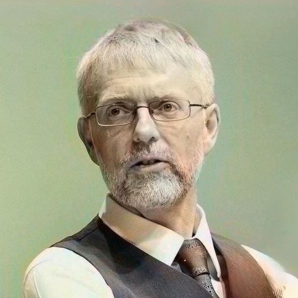 A middle-aged man with glasses and a beard, wearing a white shirt, dark vest, and patterned tie. He has light-colored hair and is looking to the side against a green background.