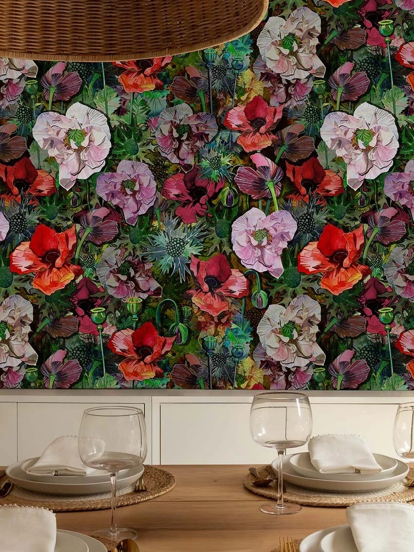 A dining table set with plates, napkins, and wine glasses in front of a vibrant floral wallpaper mural with various colorful flowers.