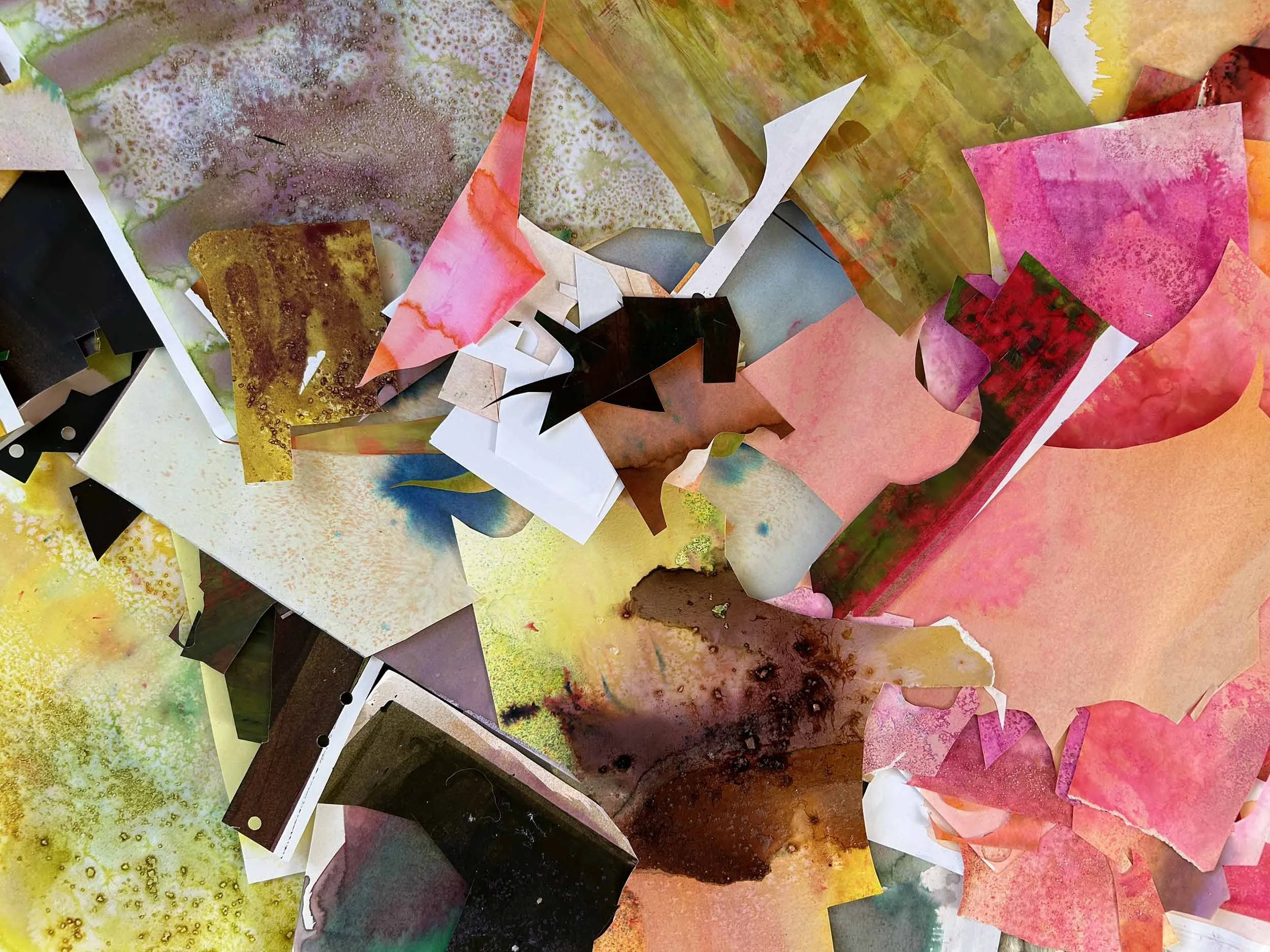 A colorful collage of watercolor paper, featuring various abstract and organic patterns in yellow, pink, green, brown, black, and purple, with some pieces torn or layered.