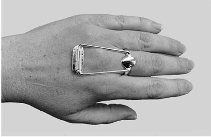 Hand resting on its side with a large safety pin attached to the middle of the fingers, appearing to hold the fingers together.