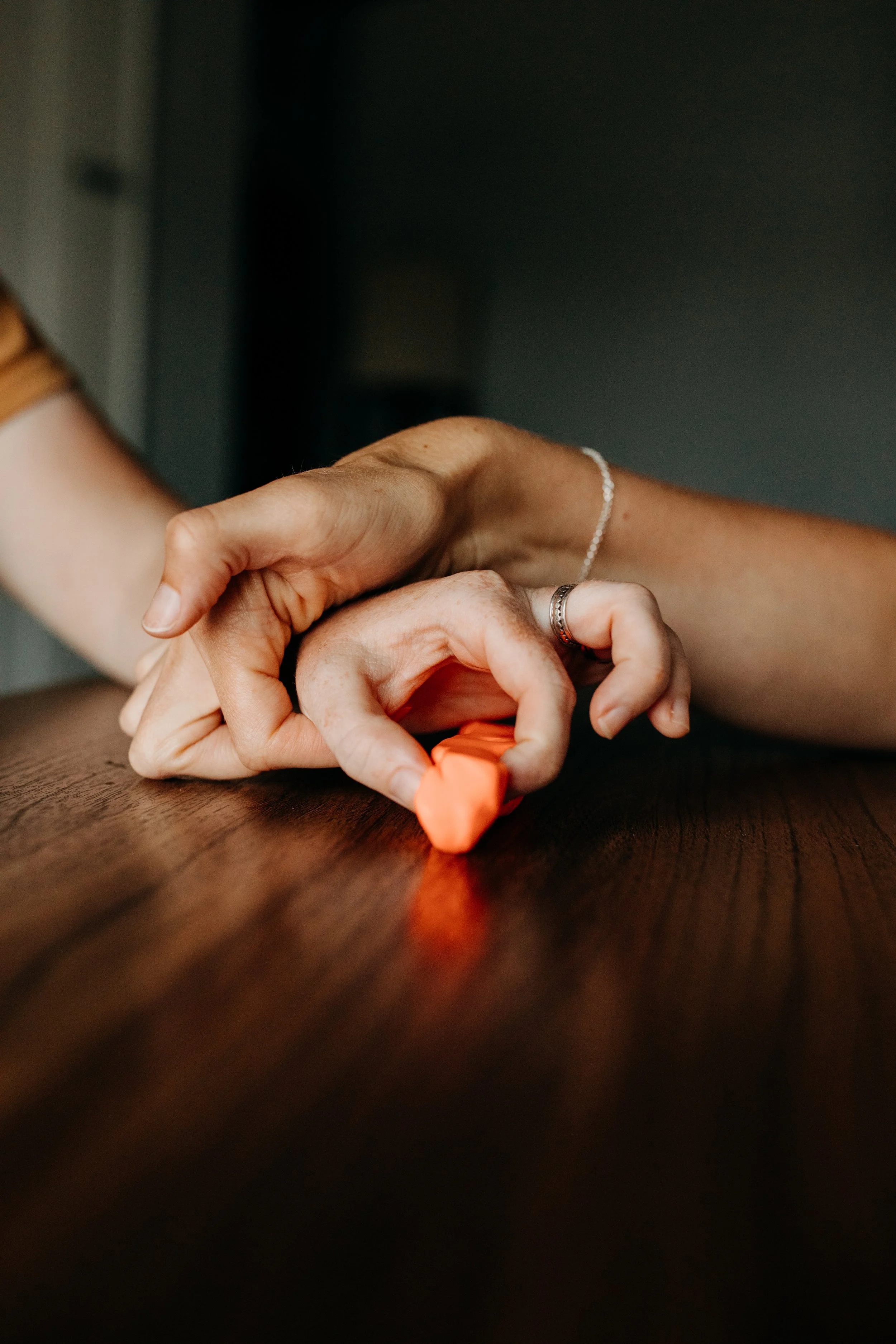 Close-up of two hands making a heart shape with a small orange object on a wooden surface.