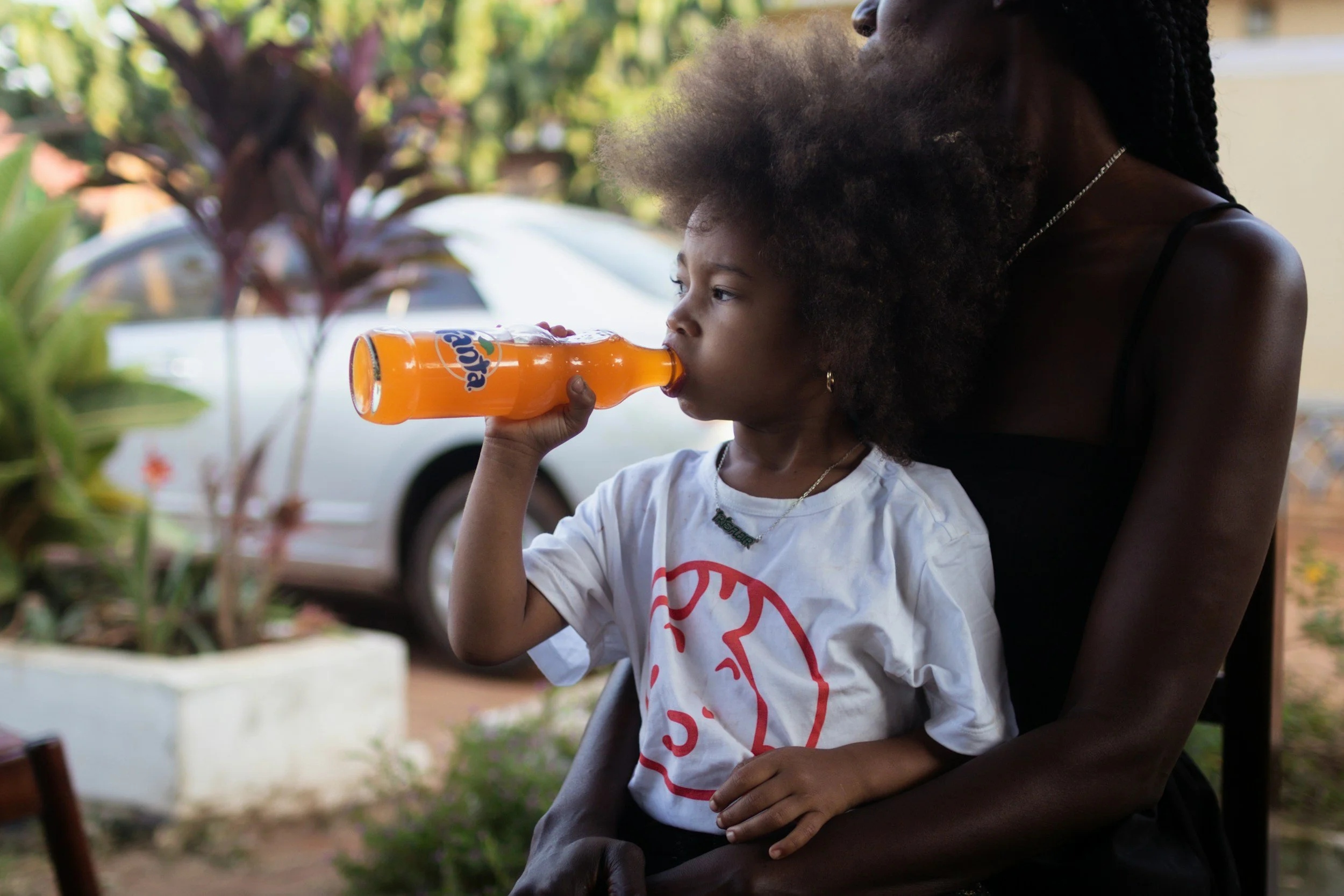 Ein kleines Mädchen trinkt afrikanische Fanta, während eine Frau es im Hintergrund hält.