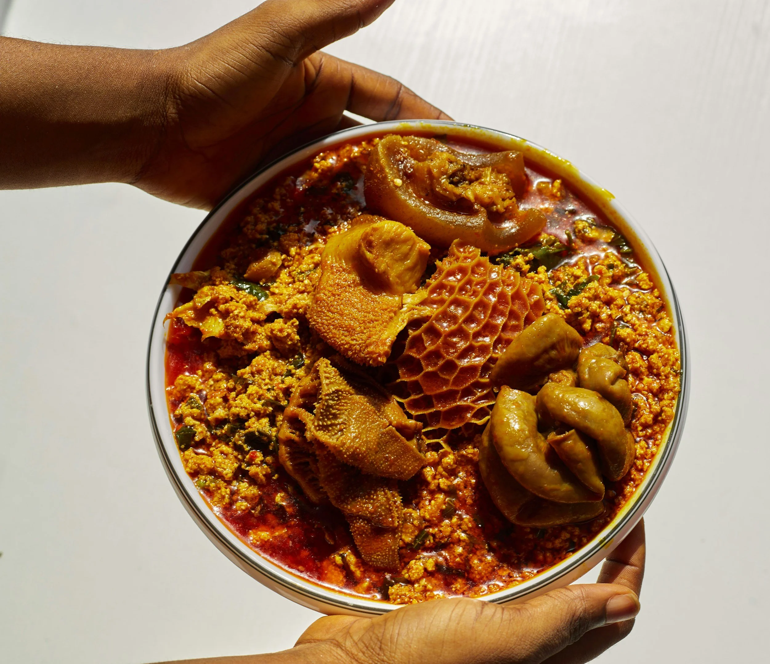 Hand hält Schüssel mit Eru und Fleisch in einer roten Soße, typische ghanaische Mahlzeit