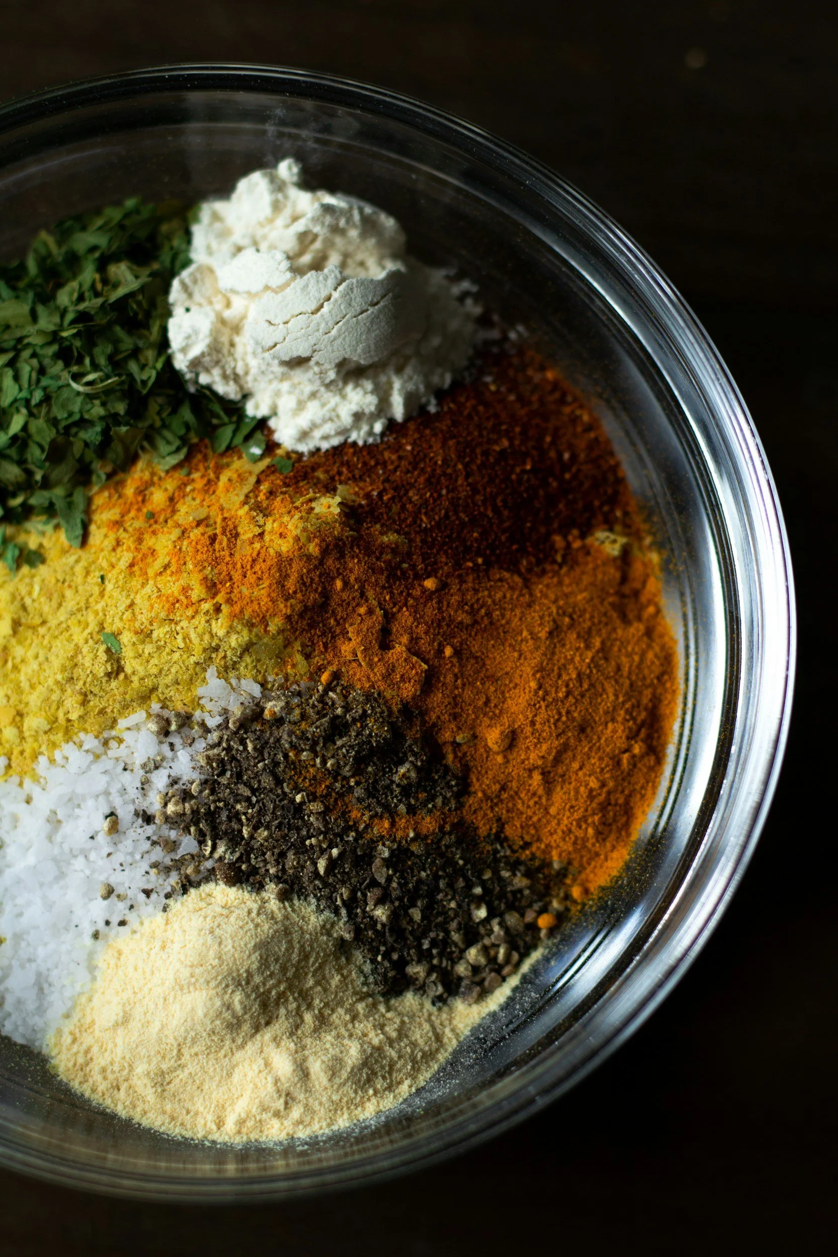 Verschiedene Gewürze in einer Glasschüssel, darunter Salz, Pfeffer, Kurkuma, Paprika, getrocknete Kräuter und Knoblauchpulver.