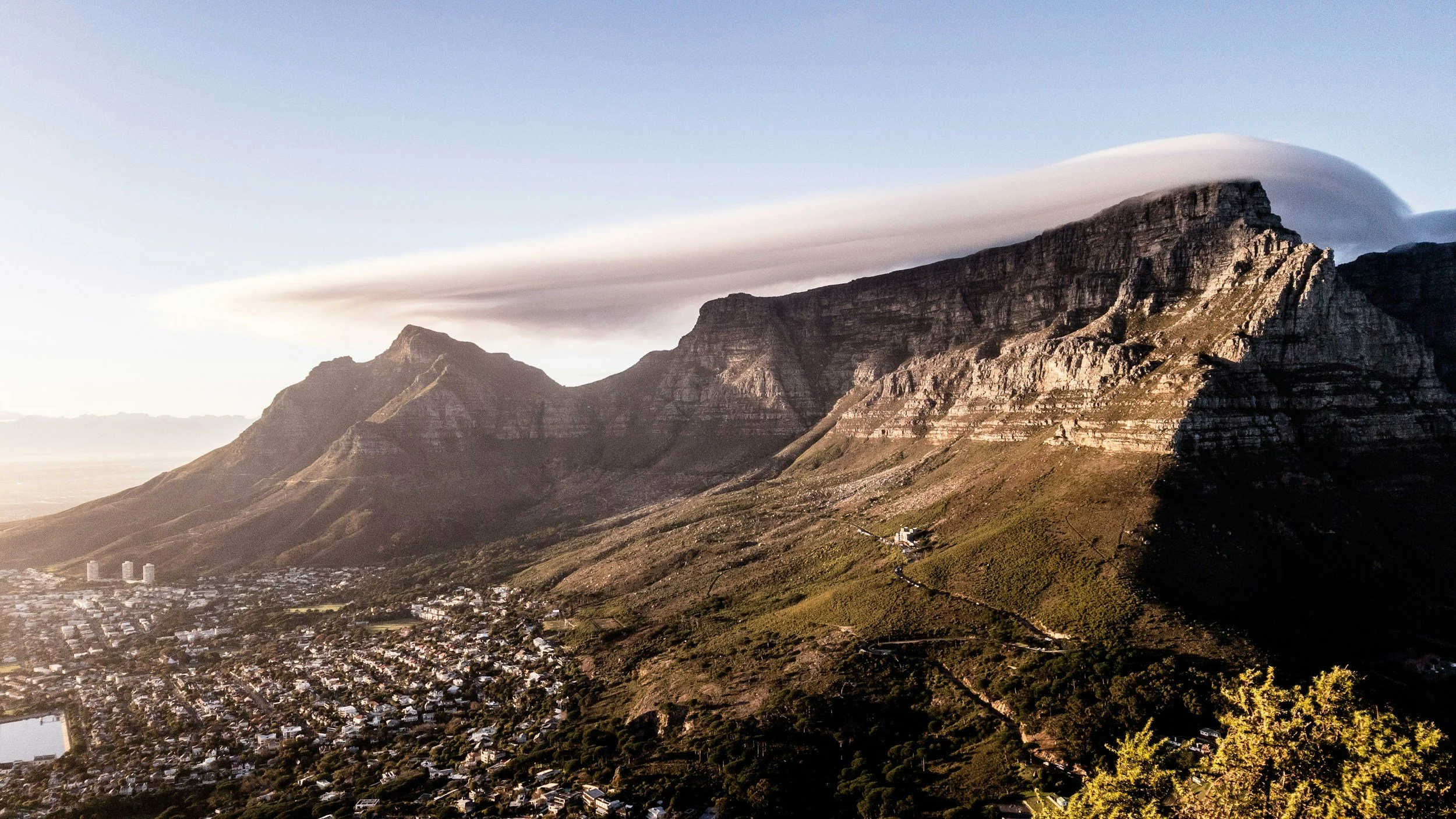 A panoramic view of Table Mountain with its iconic "tablecloth" cloud formation overlooking the city, a highlight of MGG Tours And Shuttle's private guided sightseeing and transport services in Cape Town.