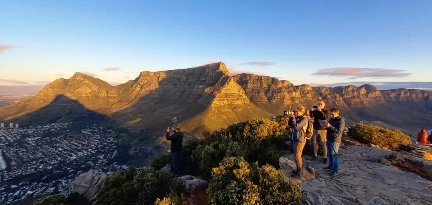 Tourists taking photos of Table Mountain at sunset from Lion's Head summit, a signature experience included in MGG Tours And Shuttle's private Cape Town city and mountain sightseeing excursions.