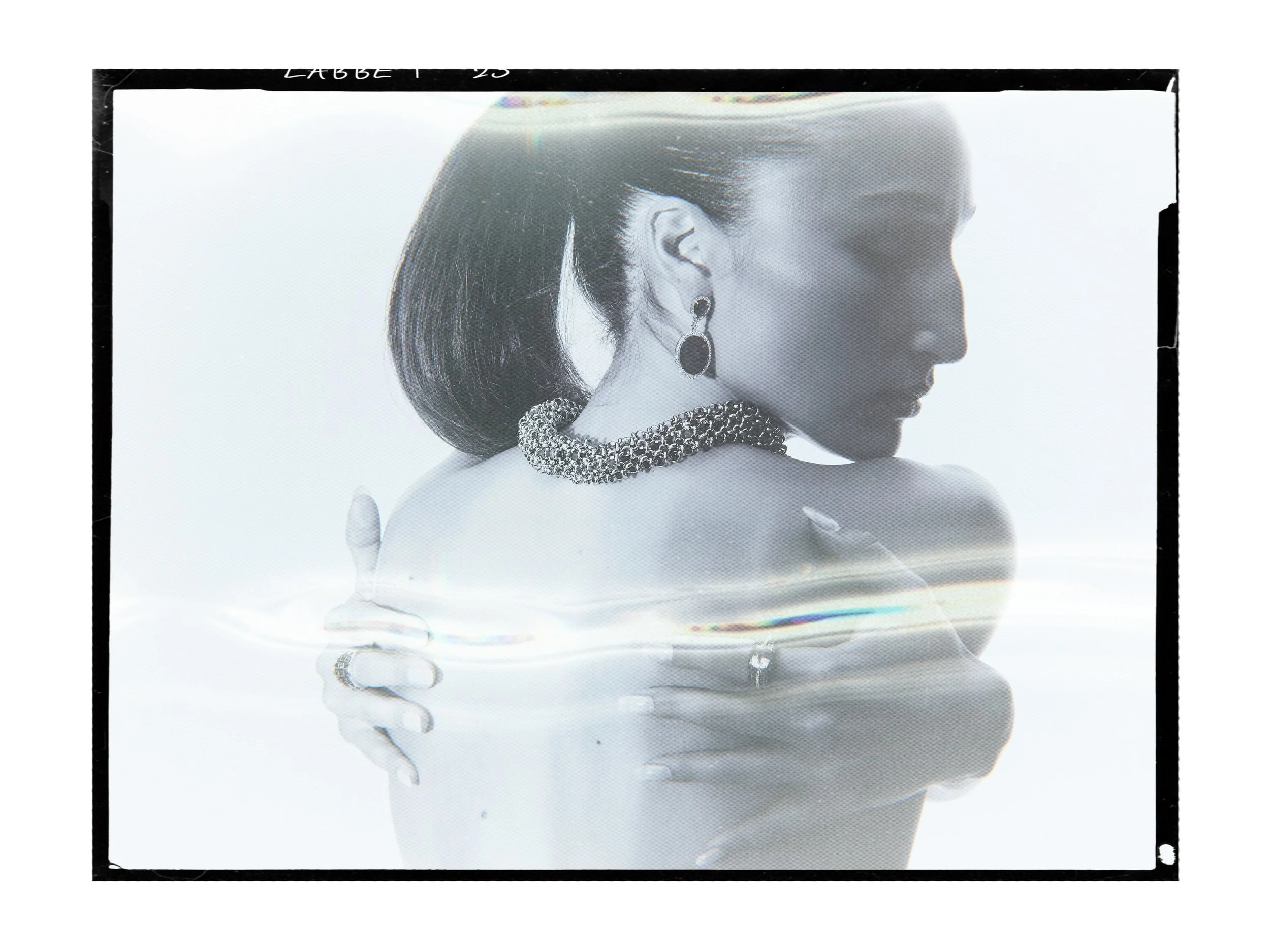 Black and white analog portrait of a woman looking over her shoulder, wearing a chunky chain necklace and drop earring

