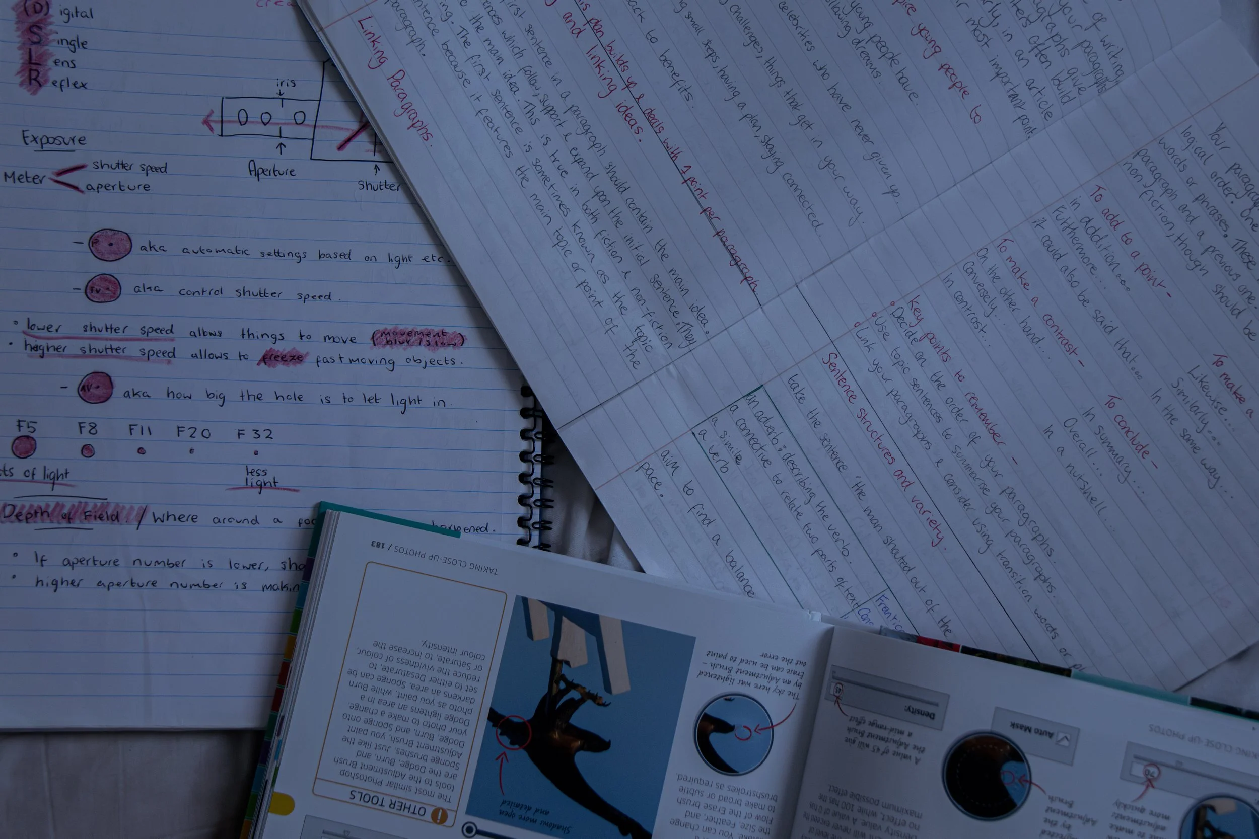 A collection of handwritten notes and diagrams related to photography, including explanations of exposure, aperture, shutter speed, ISO, and examples of camera settings. There are also printed instructional pages amid the handwritten notes.