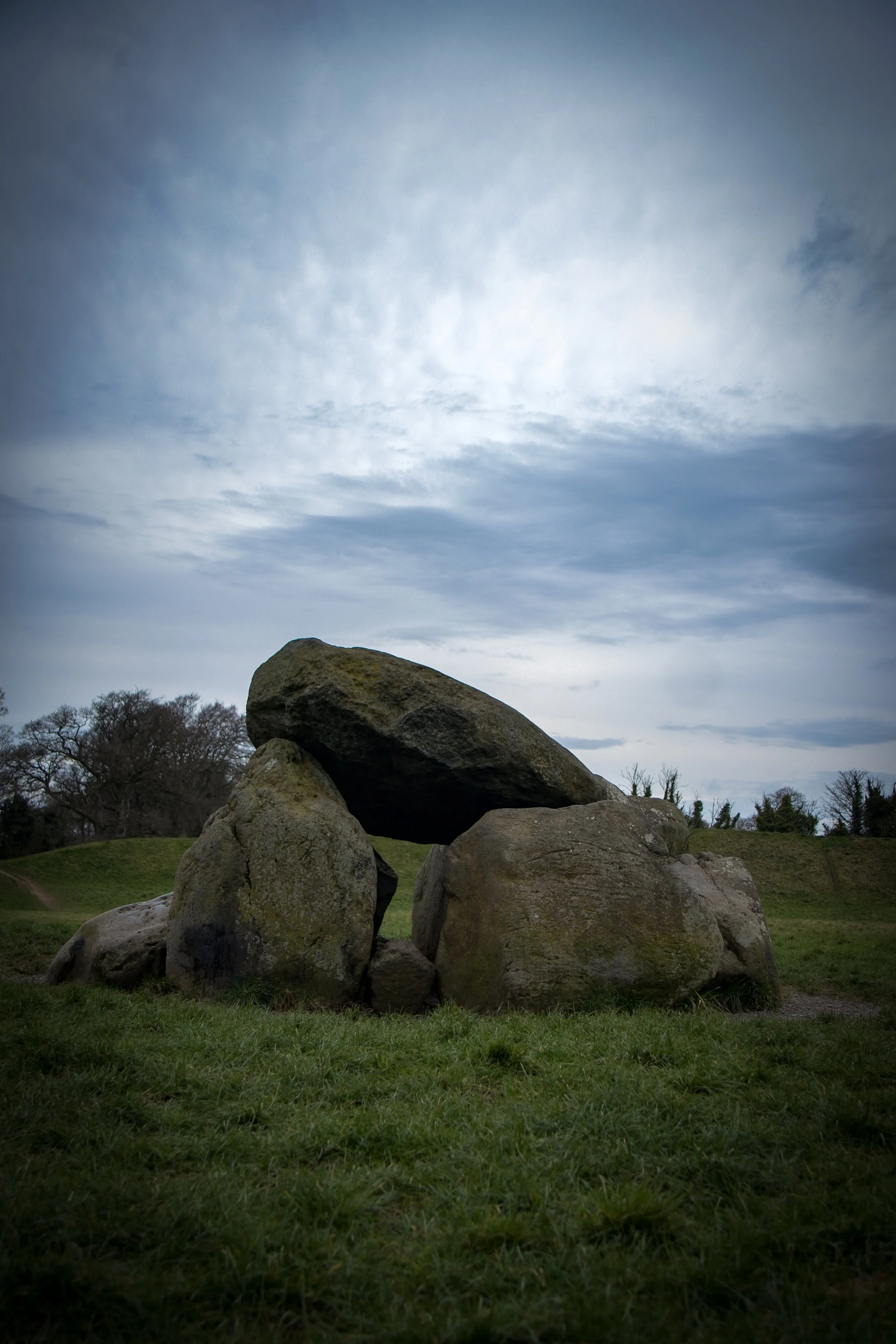 Large rocks stacked on grassy land with a cloudy sky overhead.