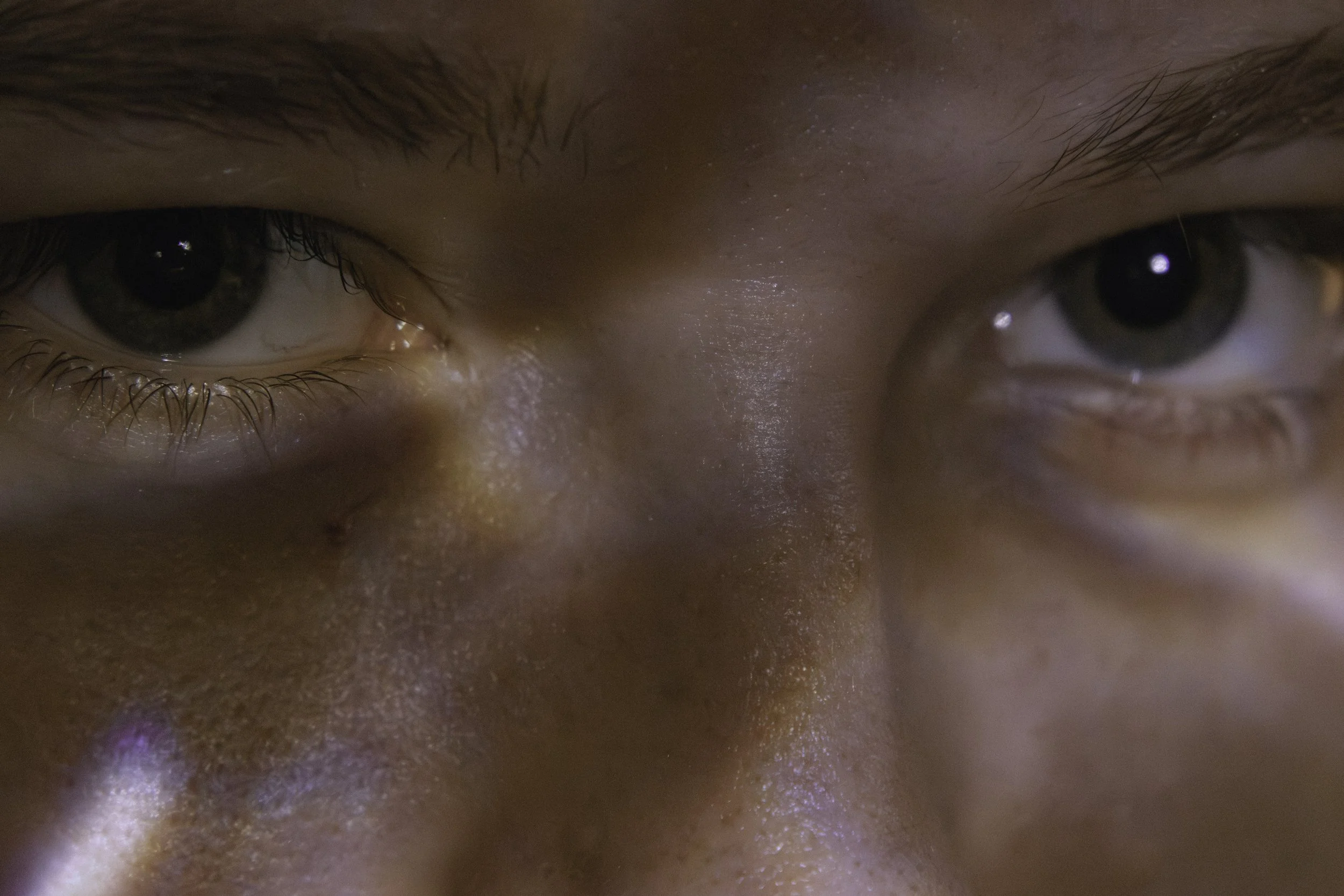 Close-up of a person's eyes and upper nose area, showing detailed skin texture and eyelashes.