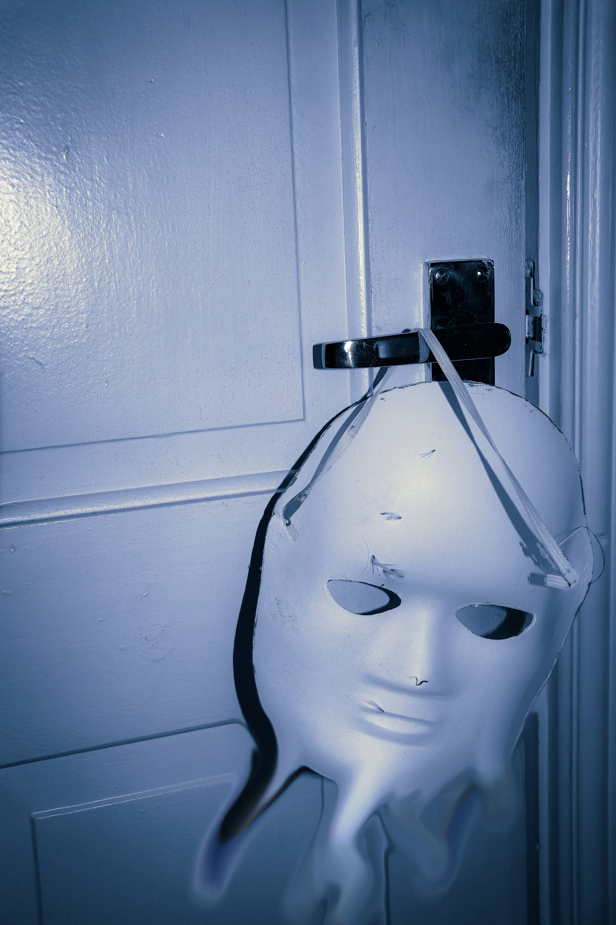 A white paper lantern hanging from a door handle by a string, with a blue painted door and wall in the background.