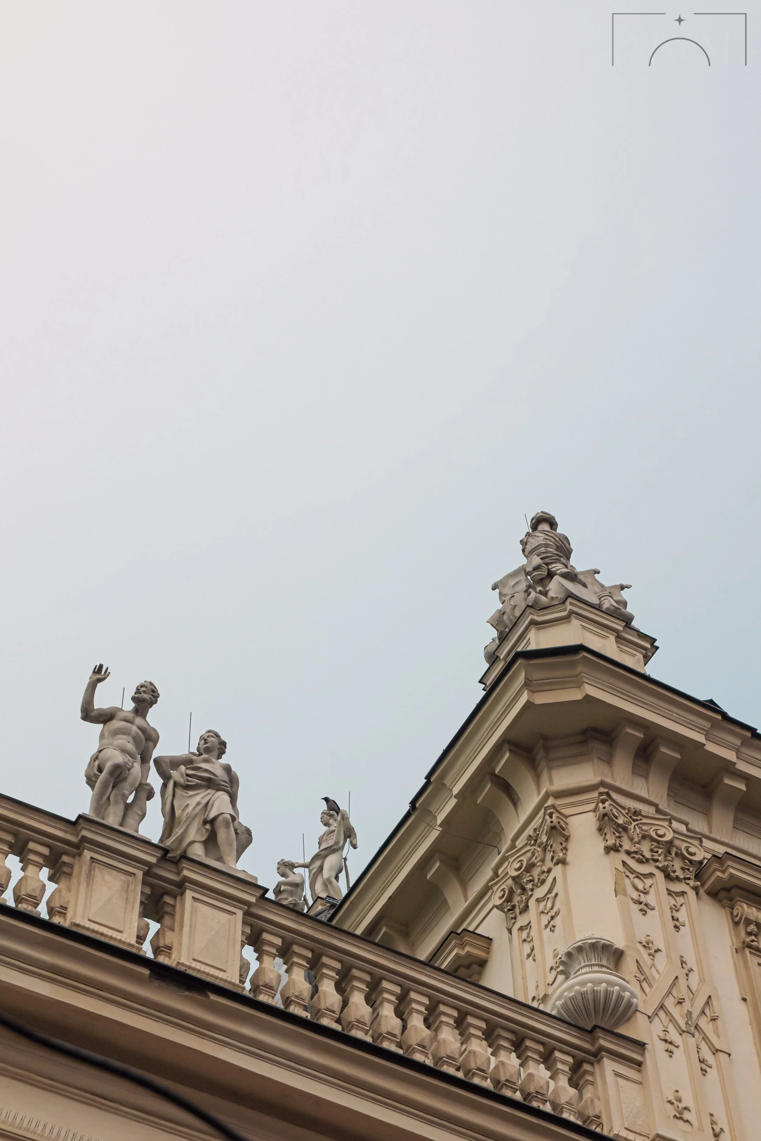 Close-up view of ornate architectural sculptures on a building roofline, including human figures and decorative details under an overcast sky.
