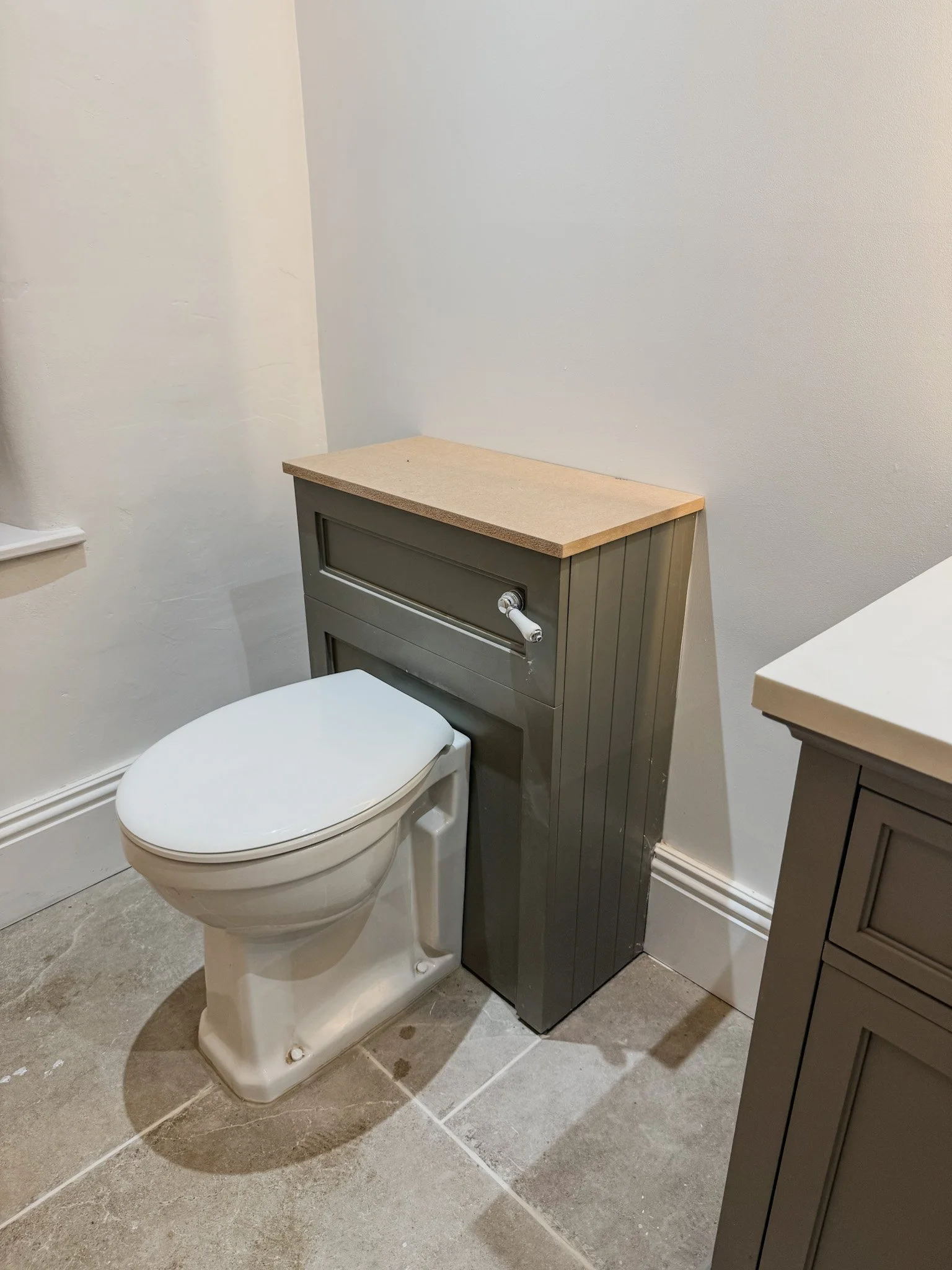 A bathroom with a toilet and a gray storage cabinet on its side with a light-colored countertop.