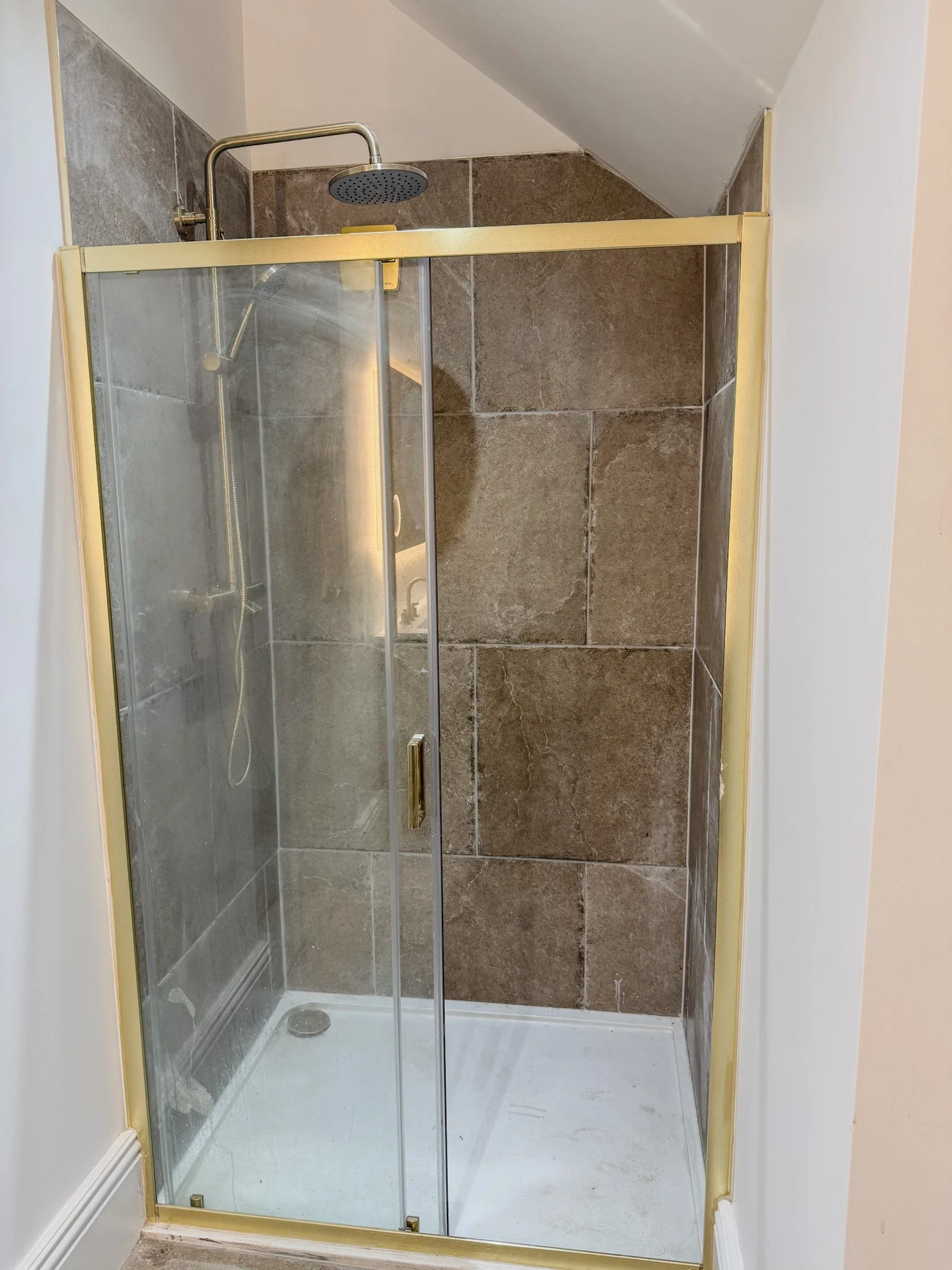 A corner shower with a glass door, brown tiled walls, and a ceiling-mounted showerhead.