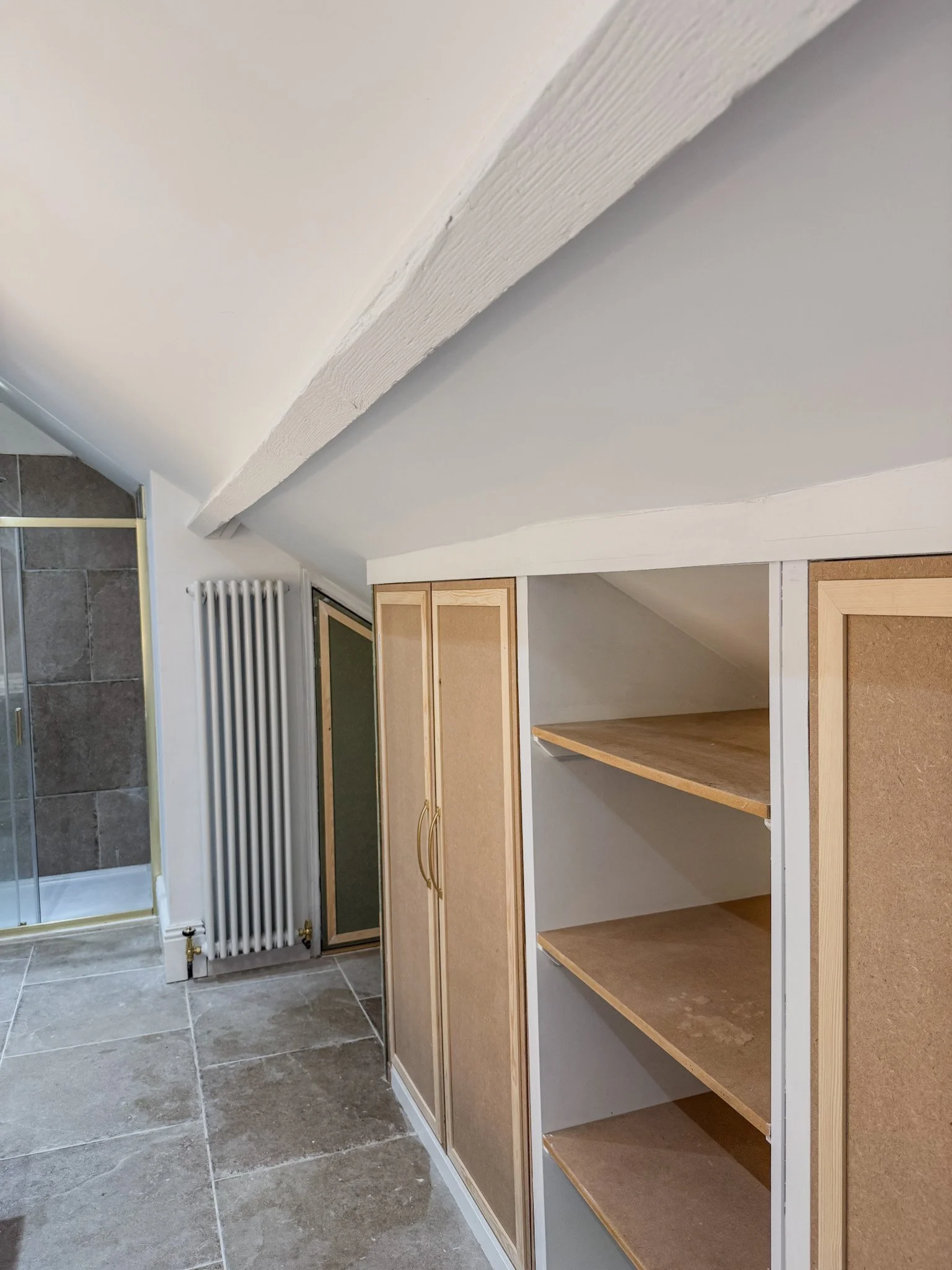 Bathroom with sliding shower door, white radiator, wooden cabinetry with open shelves, and sloped ceiling.