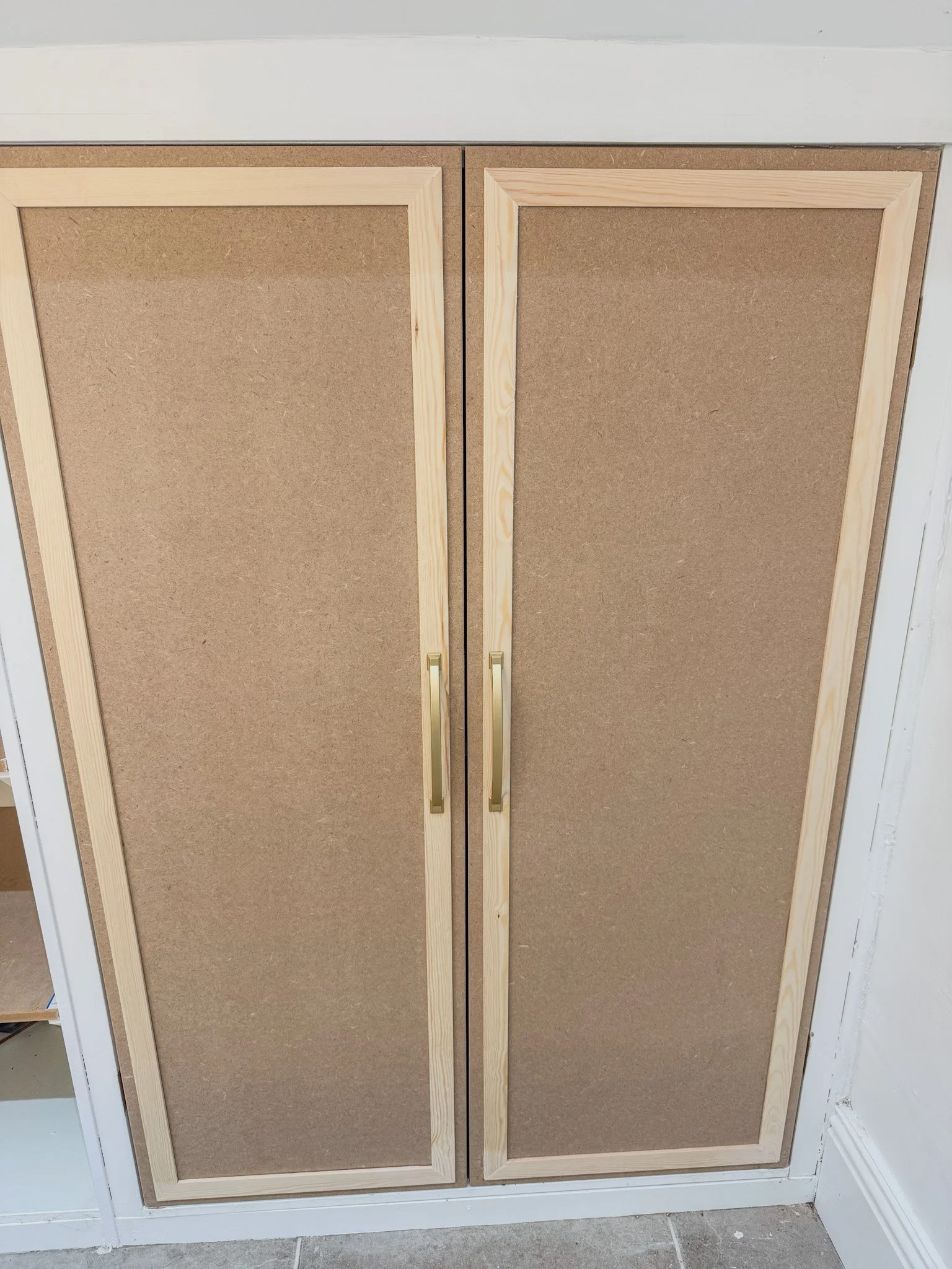 Wooden cabinet with two doors covered in brown corkboard, with gold handles.